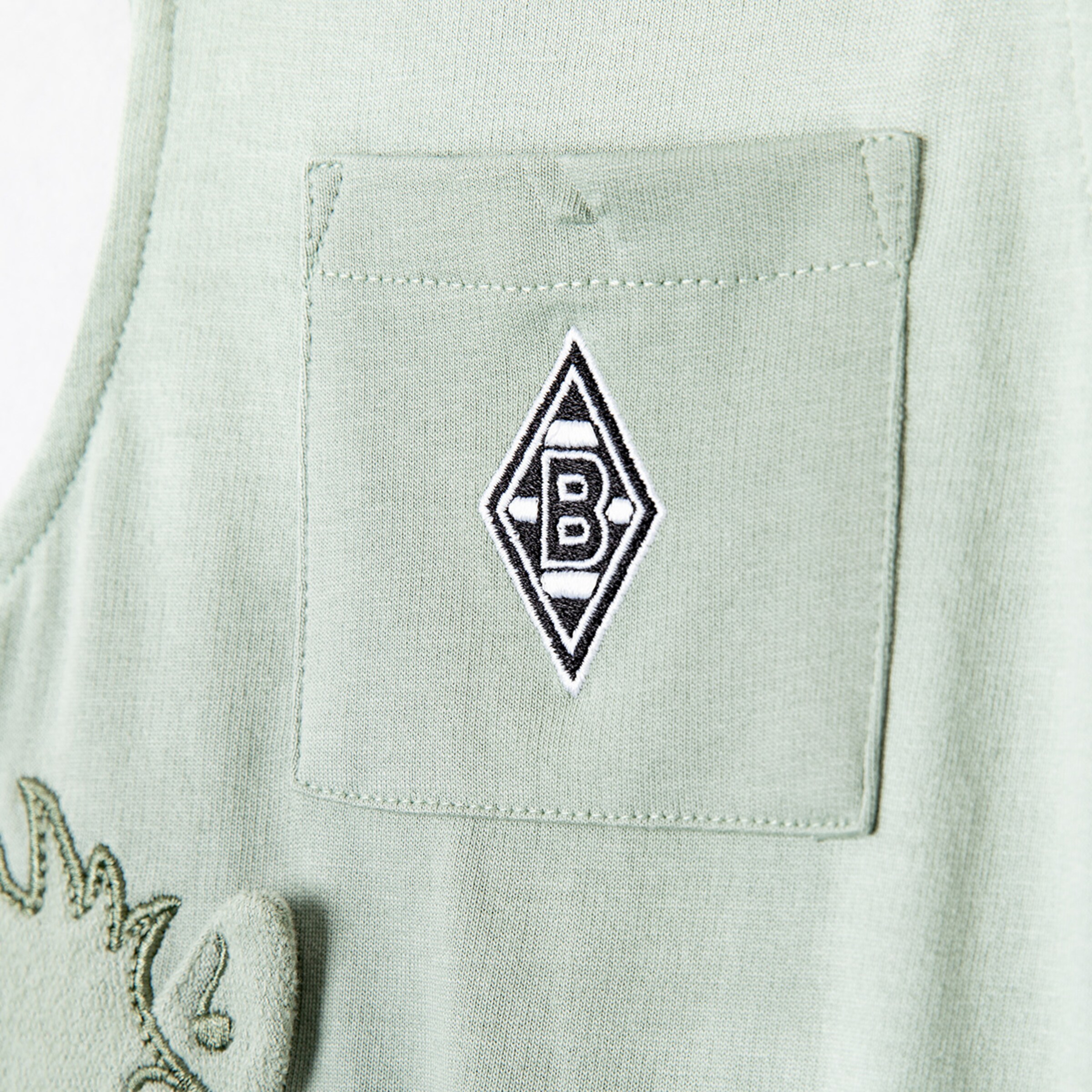 Hellgrünes Kleidungsstück mit einer Brusttasche und dem aufgestickten Rauten-Logo von Borussia Mönchengladbach.