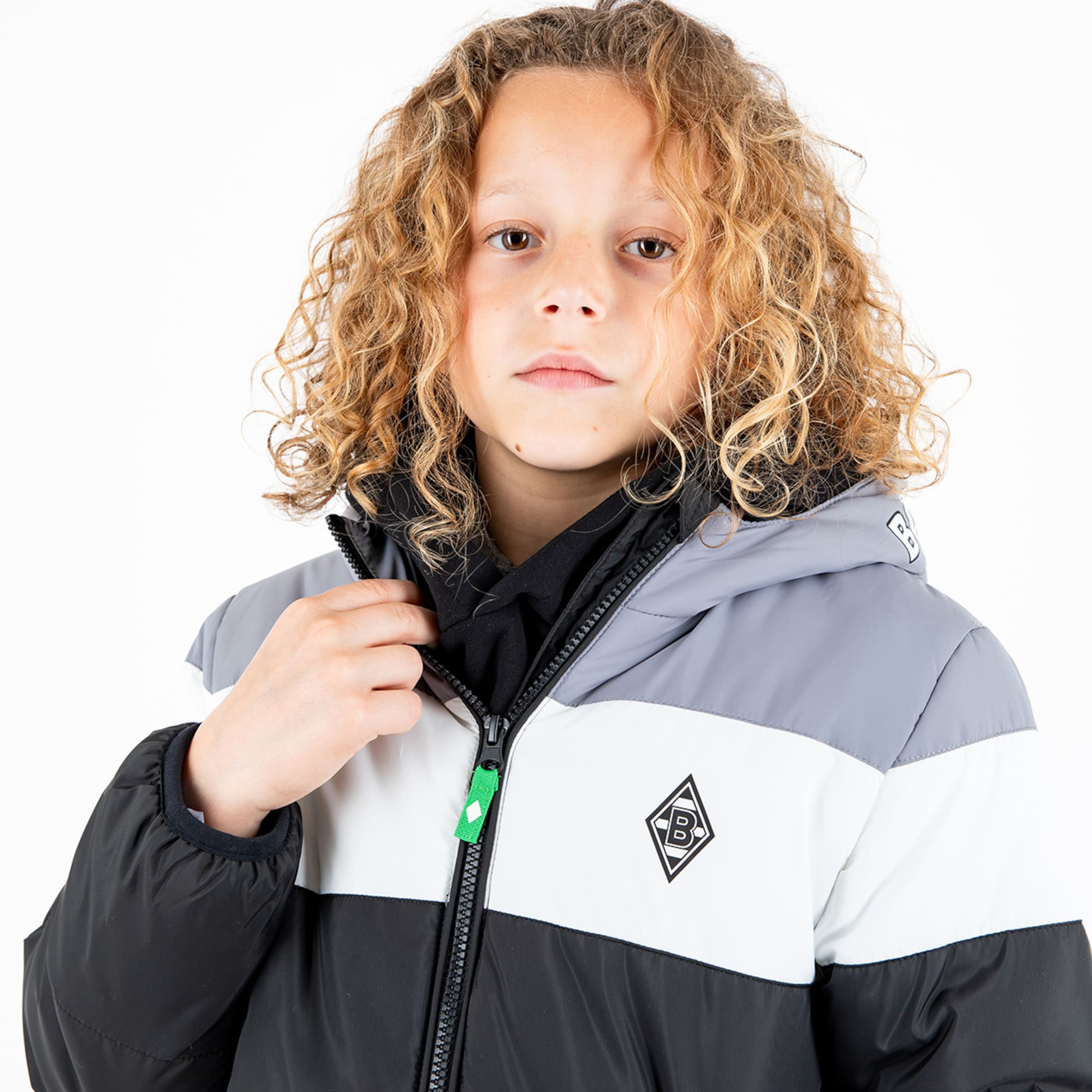A child with curly blonde hair wearing a colored jacket featuring the Borussia Mönchengladbach logo.