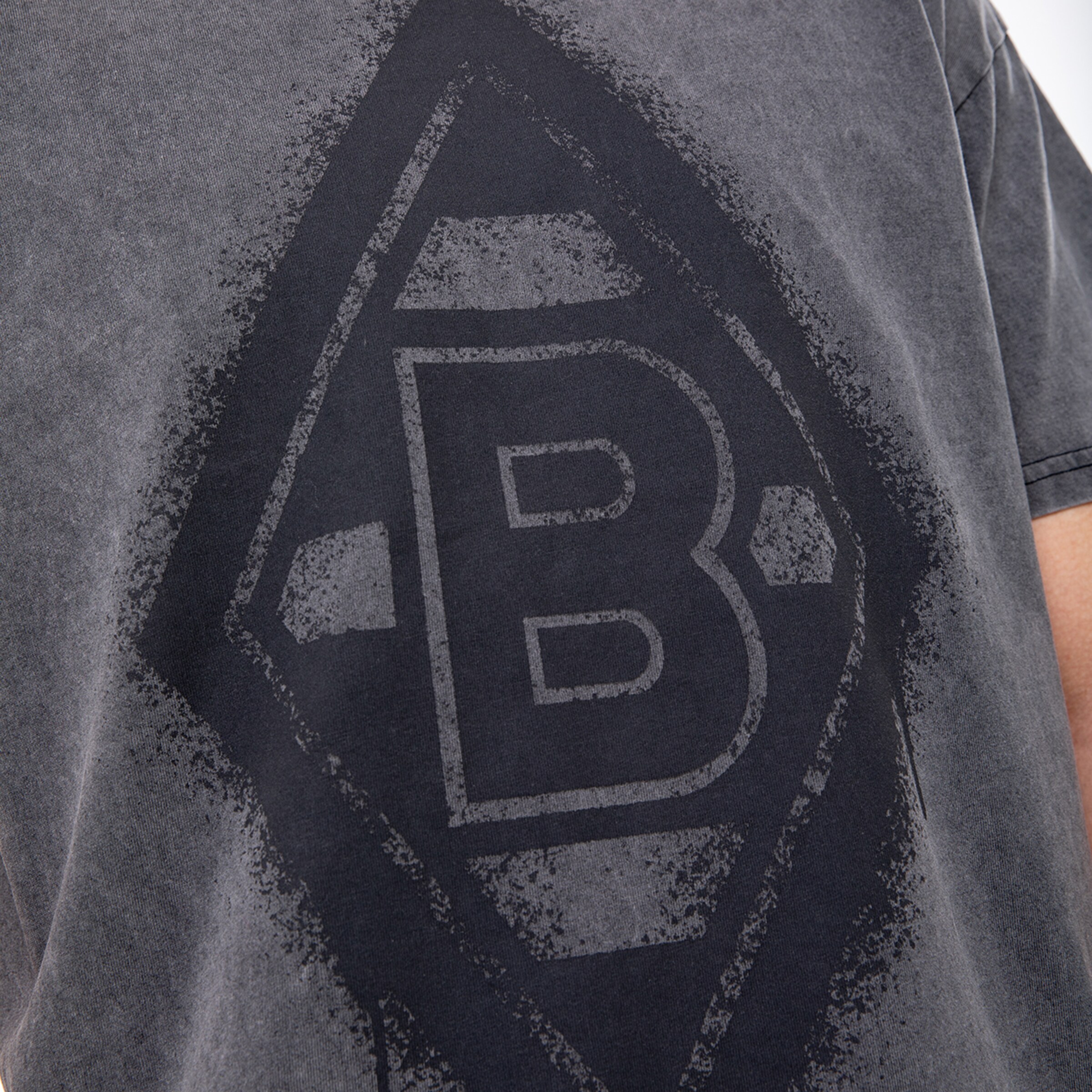 Detailansicht eines T-Shirts mit dem Borussia Mönchengladbach Logo in schwarz auf grauem Stoff.