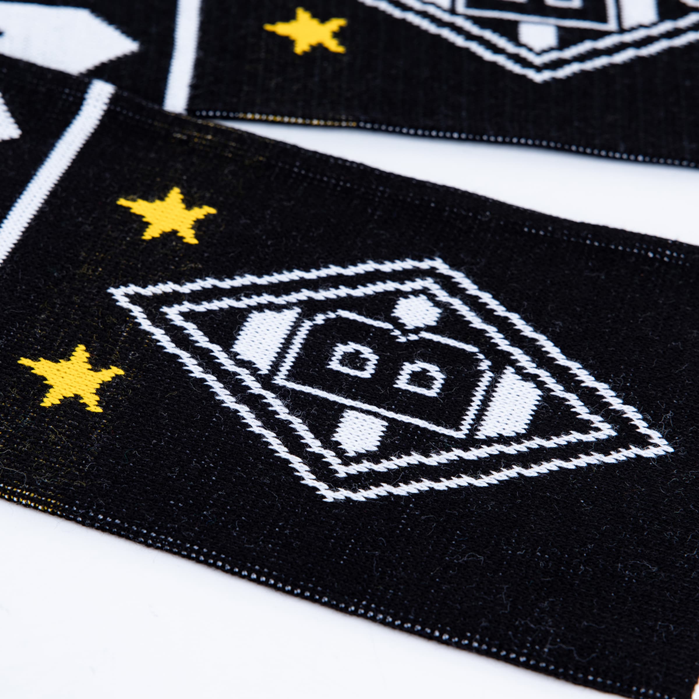 Nahaufnahme eines schwarz gestrickten Schals mit dem Logo von Borussia Mönchengladbach und zwei gelben Sternen.