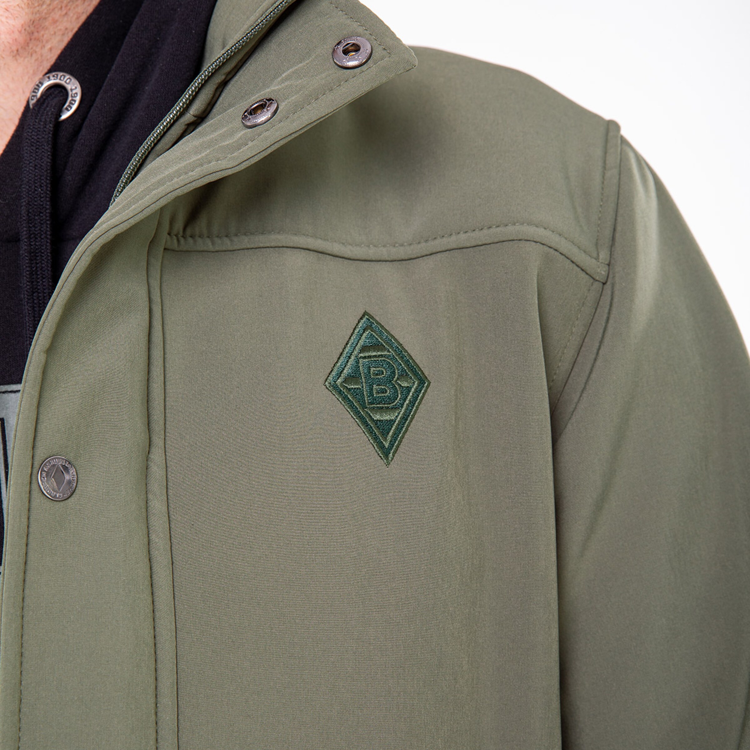 Detaillierte Ansicht einer olivgrünen Jacke mit dem Borussia Mönchengladbach-Logo.