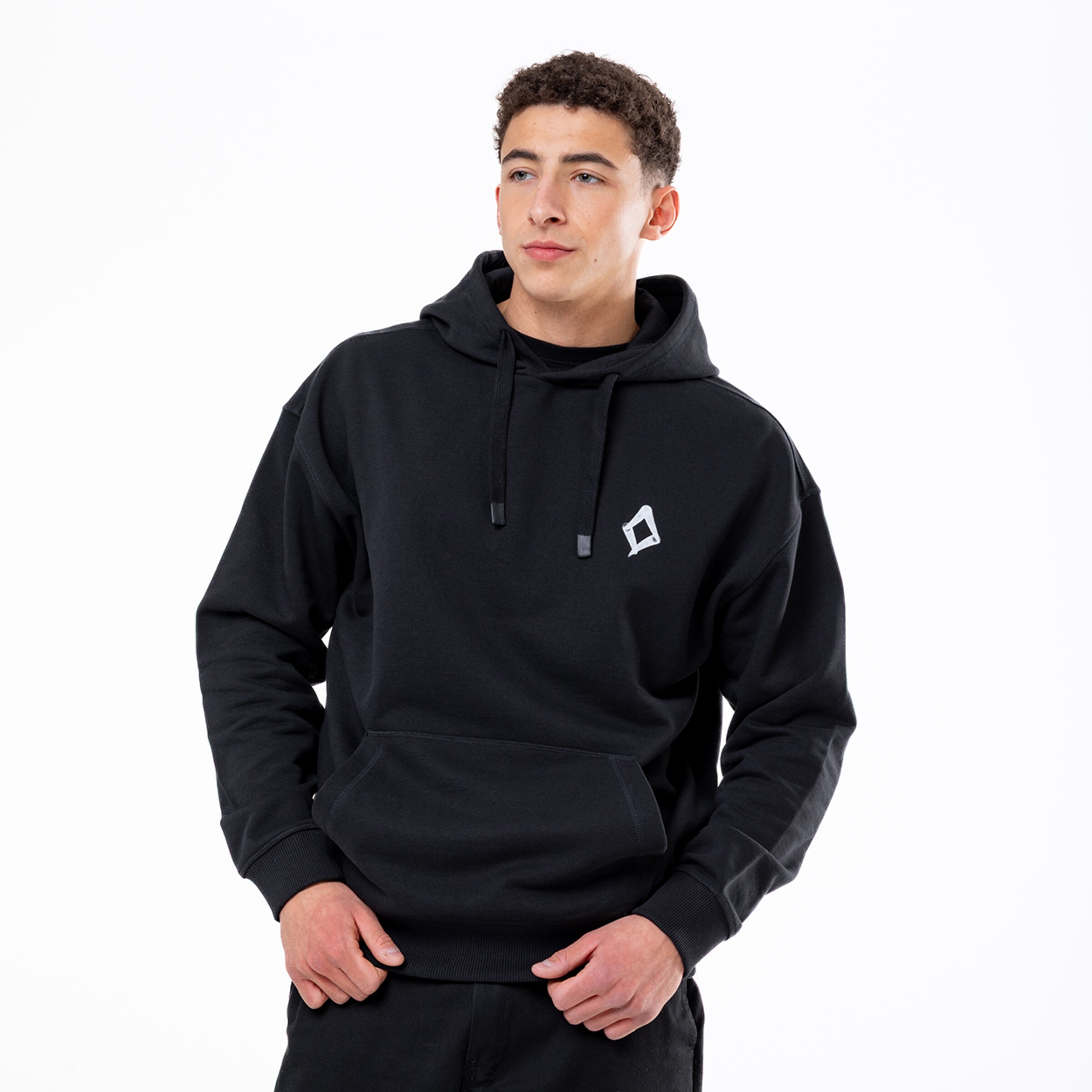 Ein junger Mann mit lockigem Haar trägt einen schwarzen Kapuzenpullover mit kleinem weißem Logo vor weißem Hintergrund.