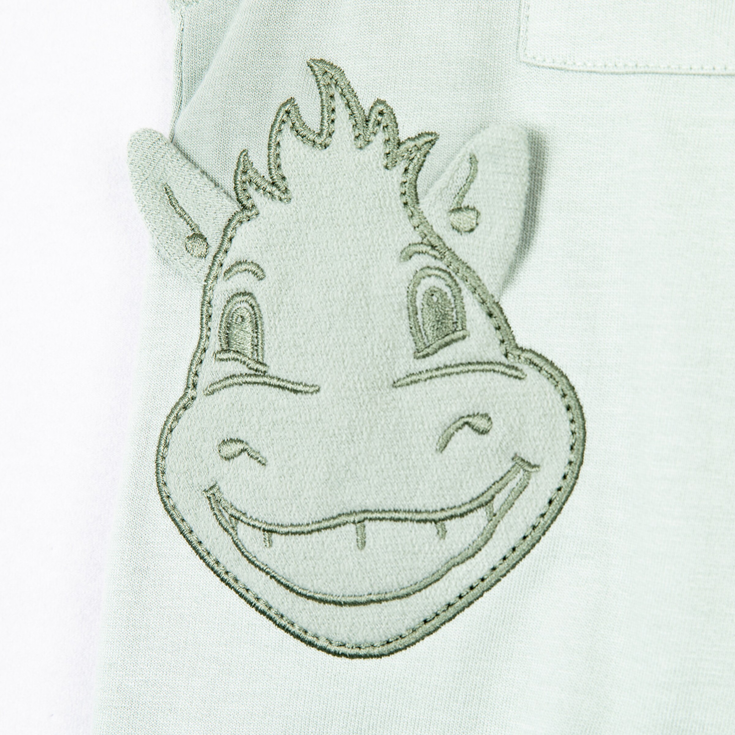 Stickerei eines lächelnden Kuhgesichts auf einem grauen Stoff.