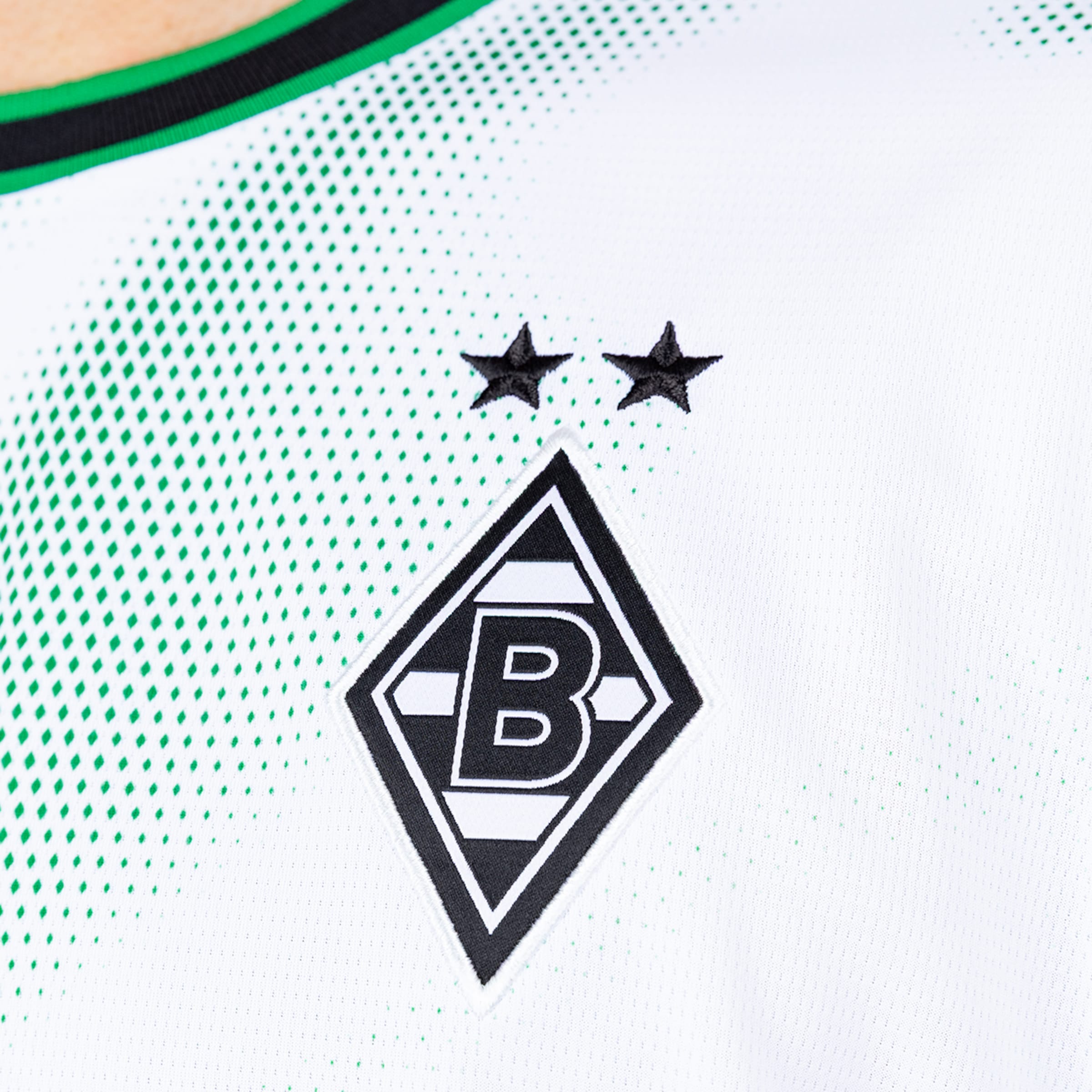 Borussia Mönchengladbach Wappen auf weißem Trikot mit grünem Rautenmuster und zwei schwarzen Sternen über dem Vereinslogo.