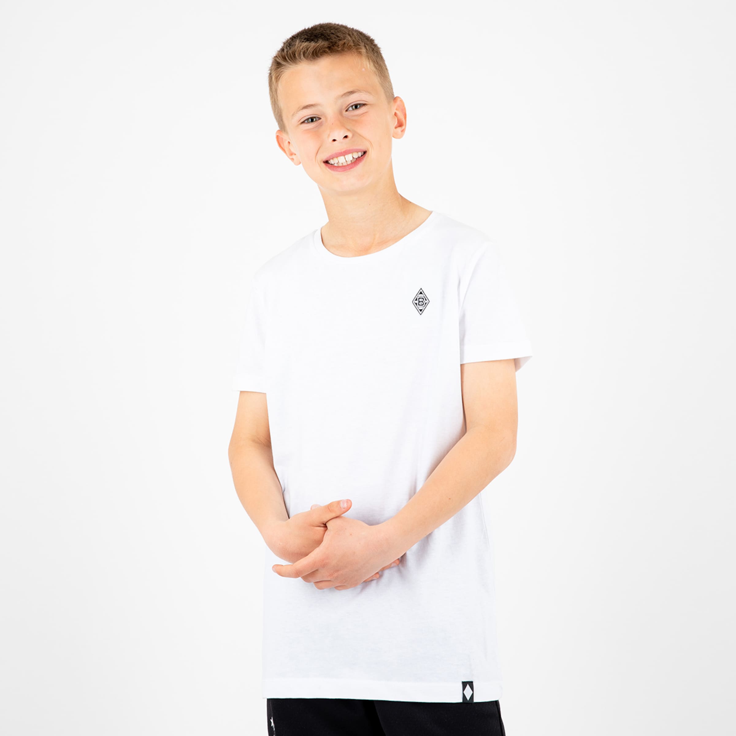 Ein Junge in einem weißen T-Shirt mit dem Borussia Mönchengladbach Logo steht lächelnd und hat die Hände vor sich verschränkt.