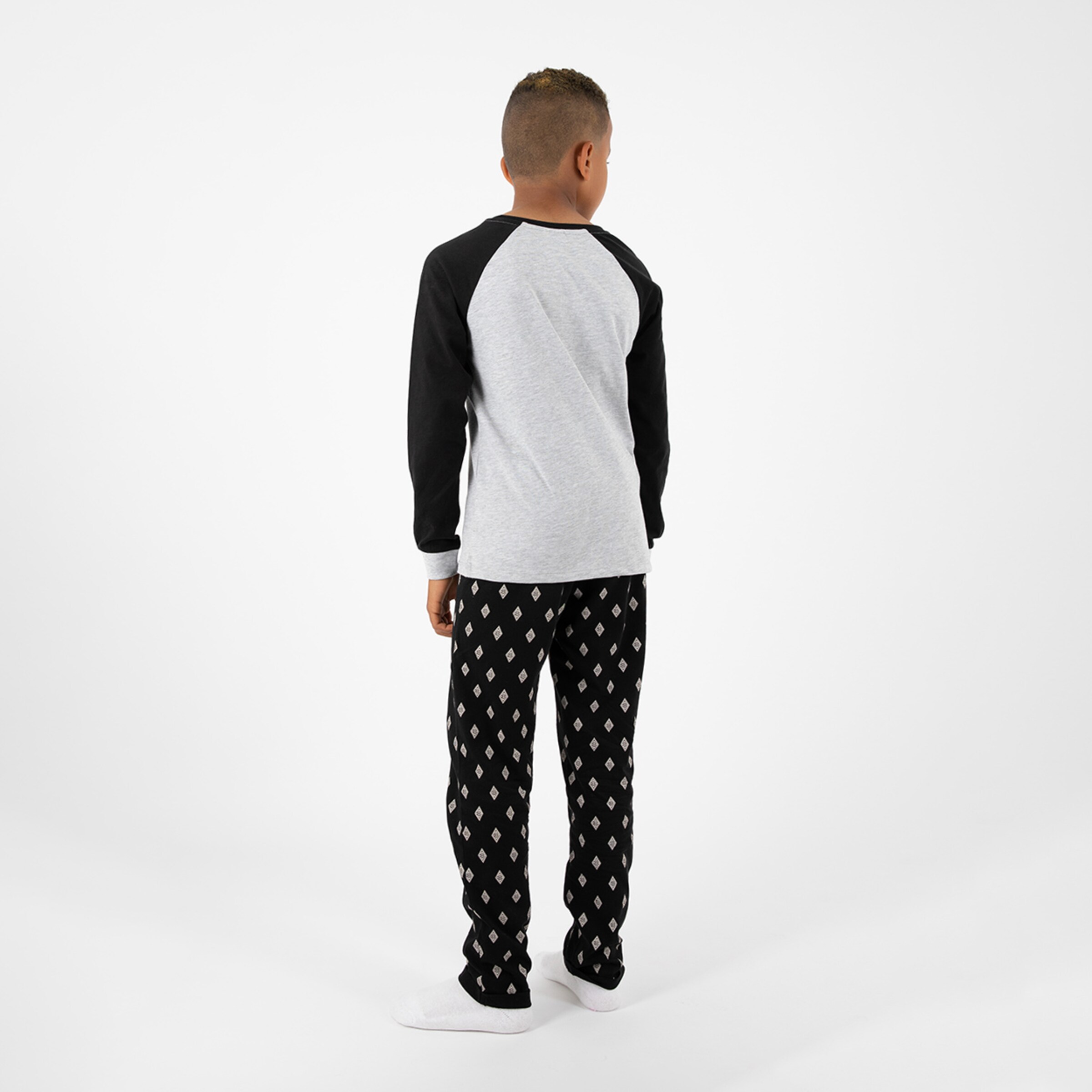 Junge trägt graues T-Shirt und schwarze Pyjamahose mit Muster von hinten gesehen.