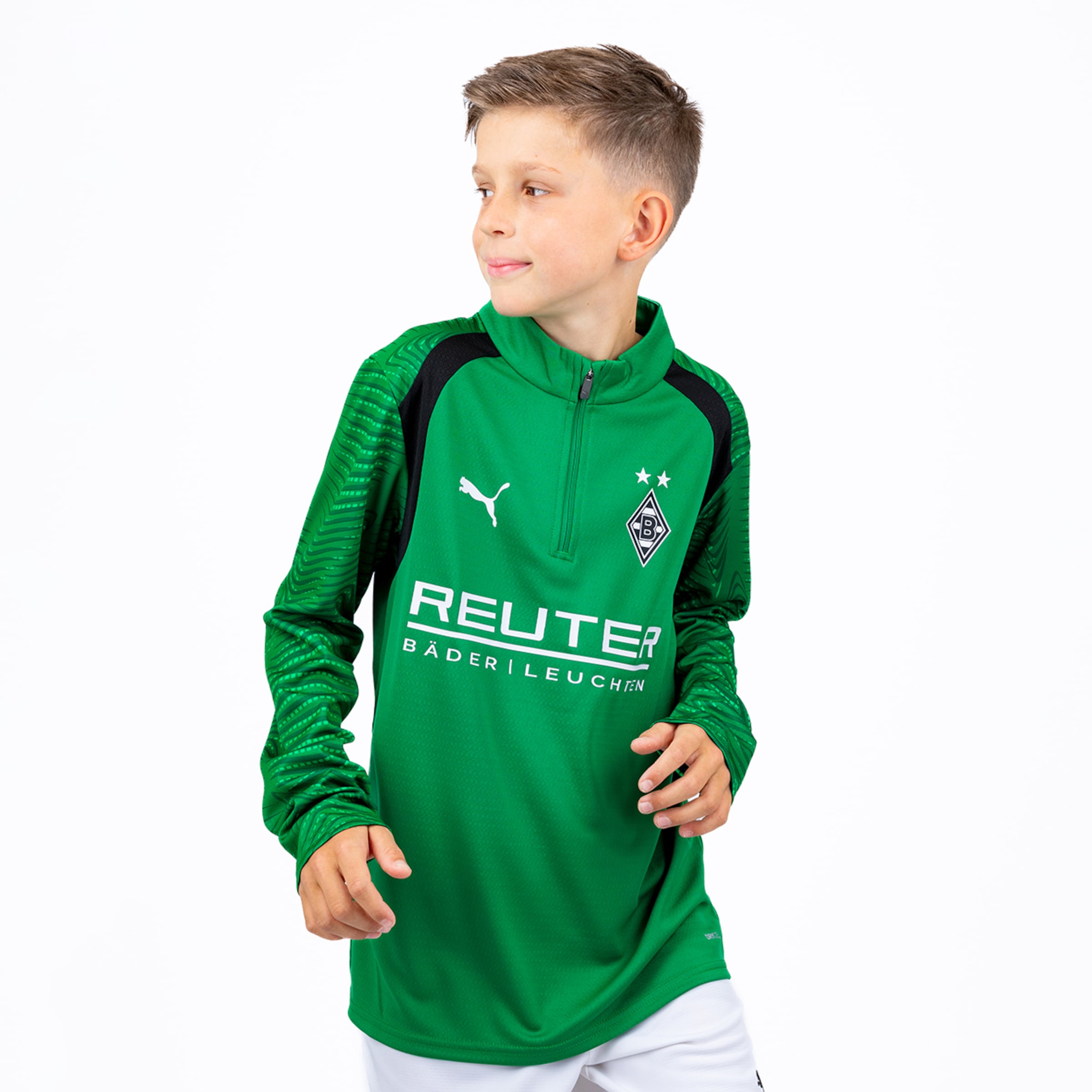 Ein junger Junge in grünem langärmeligen Sportshirt mit Puma-Logo, Reuter-Sponsor und Borussia Mönchengladbach-Wappen mit zwei Sternen, nach links blickend, vor weißem Hintergrund.
