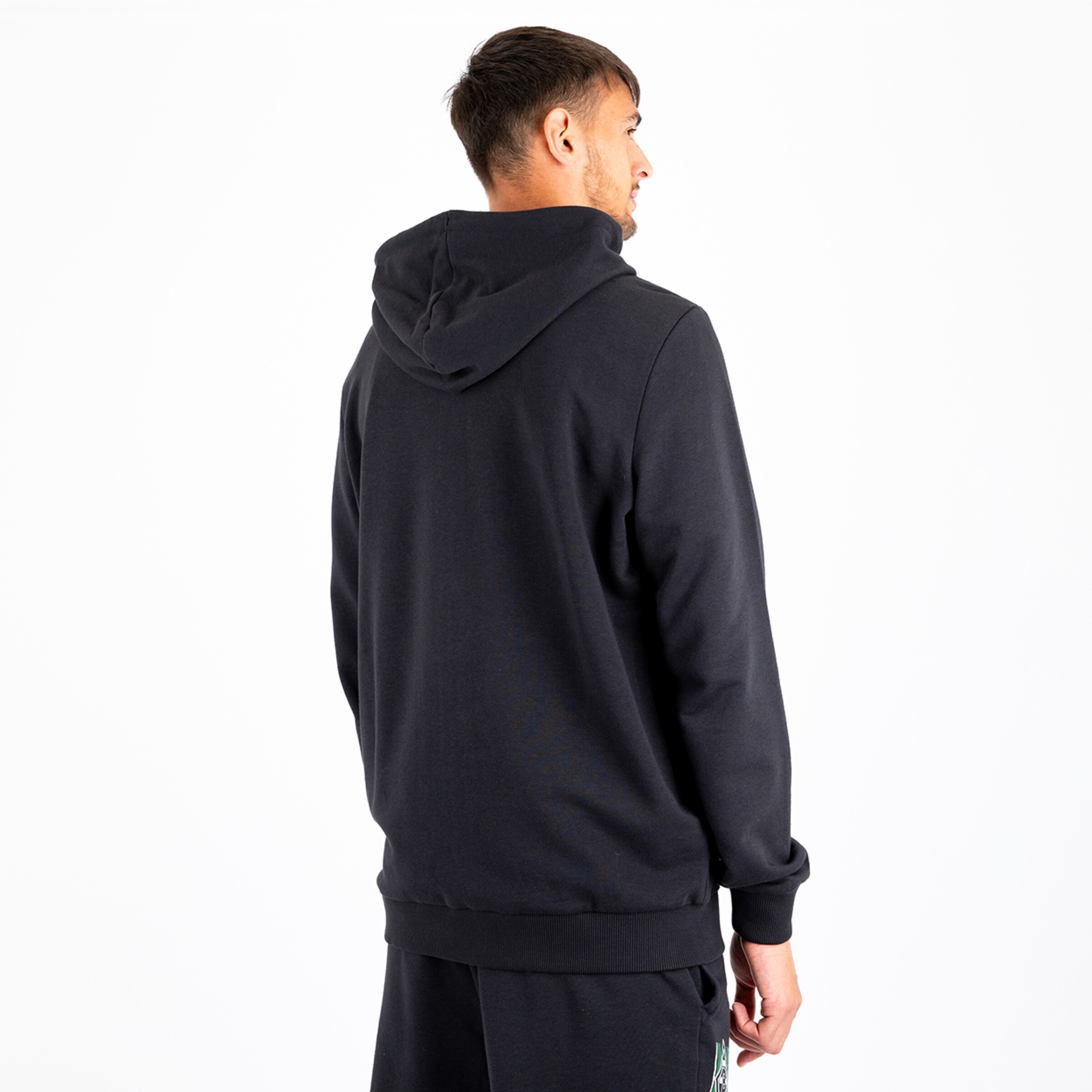 Mann in schwarzer Kapuzenjacke von hinten steht vor neutralem Hintergrund.