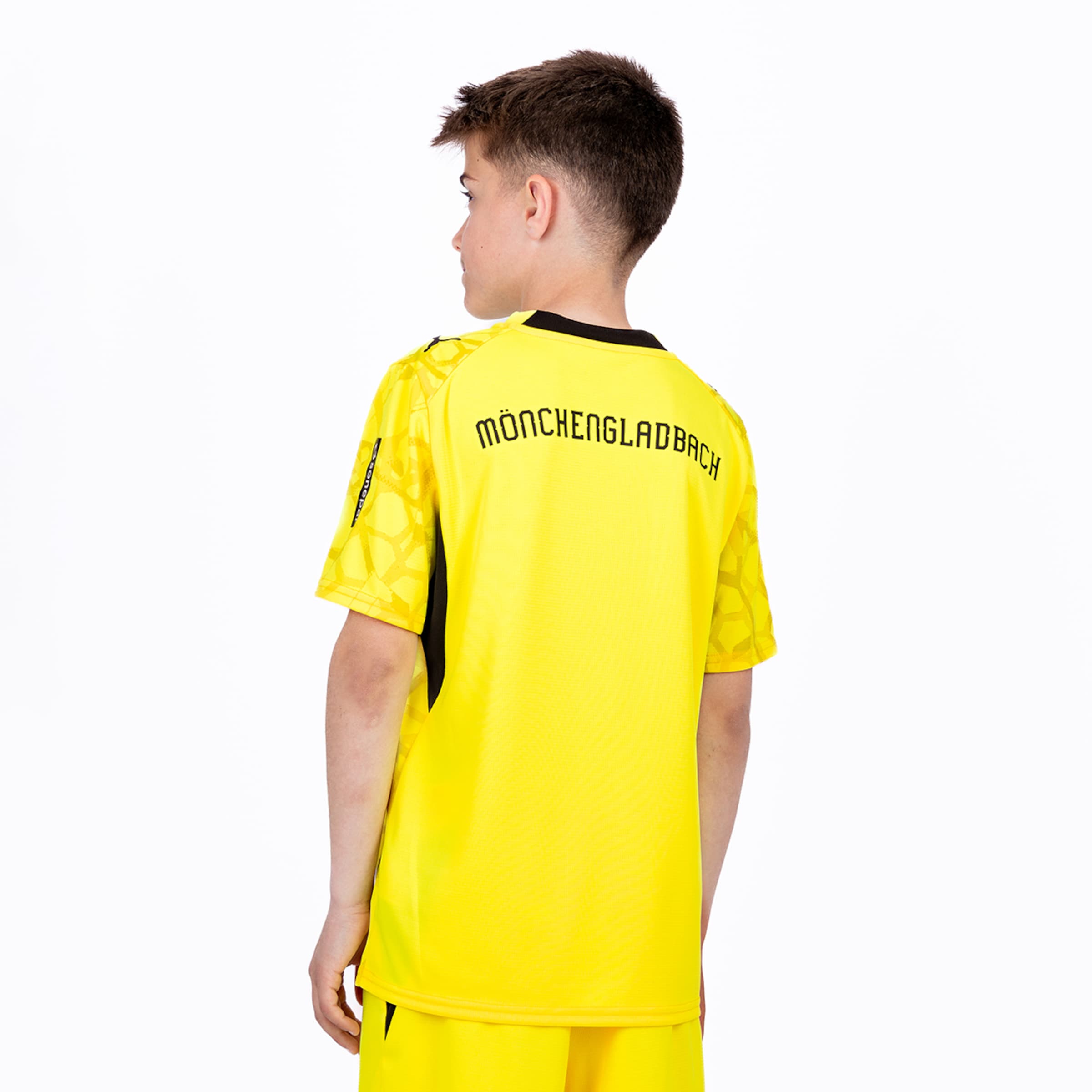 Junge von hinten in gelbem Borussia Mönchengladbach Trikot und Shorts vor weißem Hintergrund.