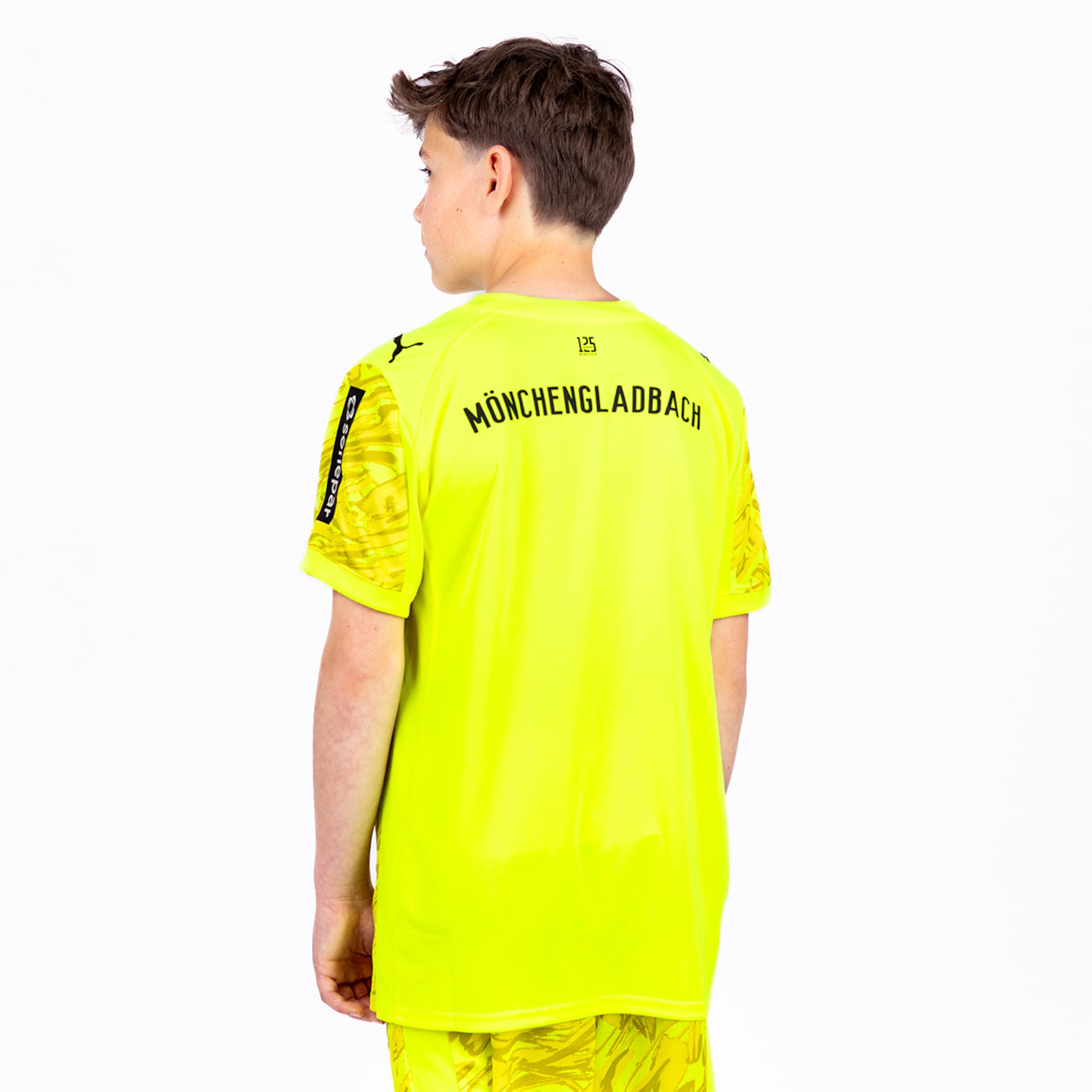 Junger Junge zeigt das Rückenteil eines gelben Mönchengladbach-Trikots mit Aufschrift.