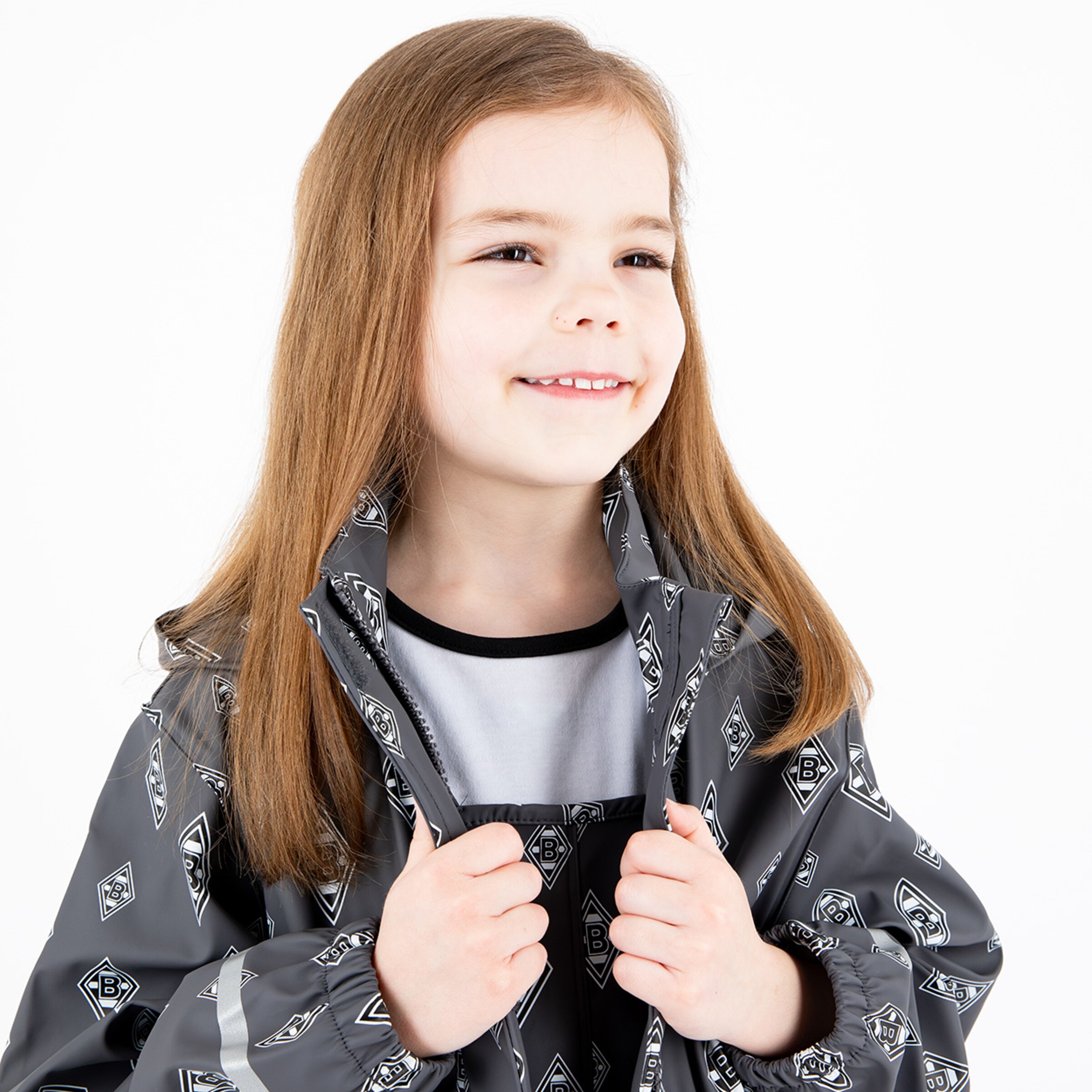 Ein Mädchen mit langen Haaren trägt eine graue Jacke mit Borussia Mönchengladbach-Logo und lächelt.
