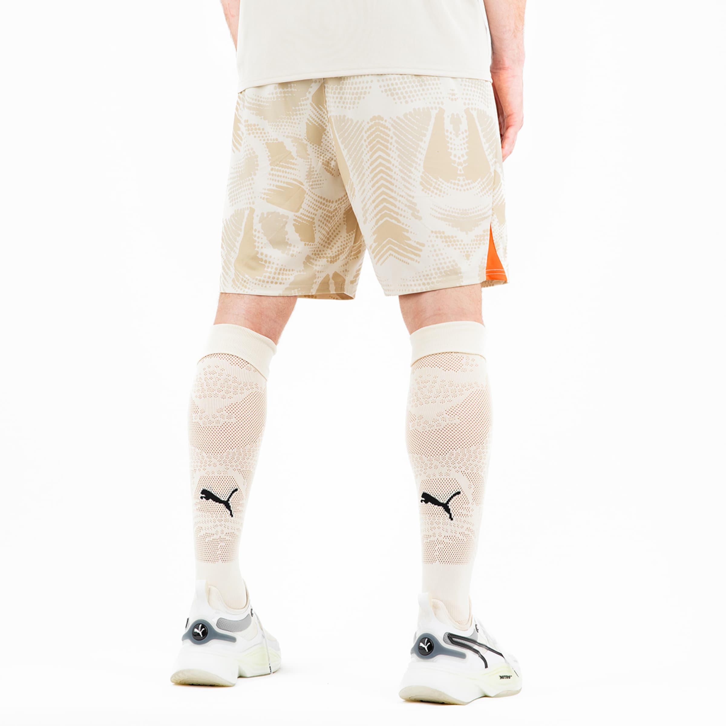 Sportliche Shorts in hellem Design mit orangen Akzenten kombiniert mit weißen Schienbeinschonern und sportlichen Schuhen.