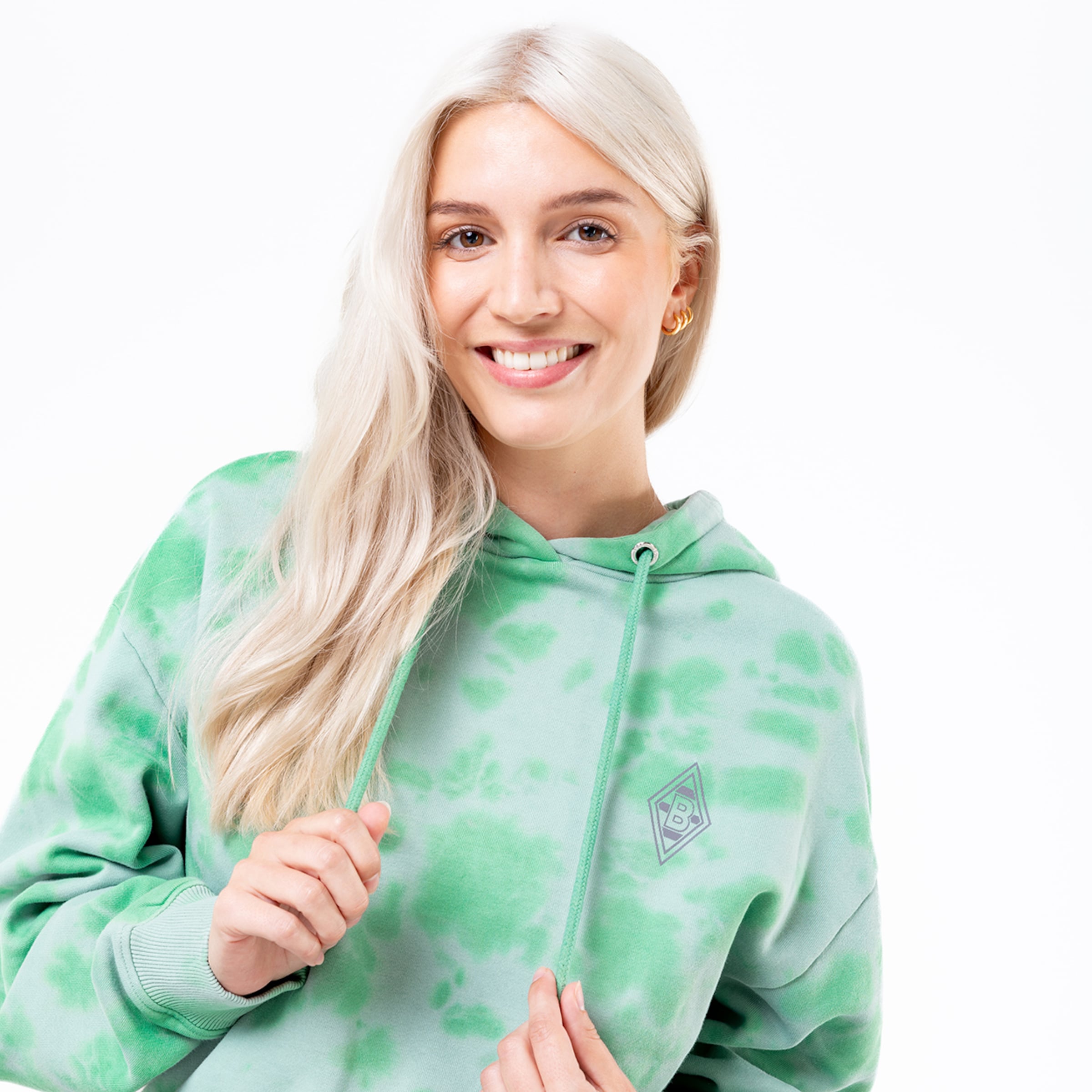 Woman with blonde hair wearing a tie-dye green hoodie and smiling.
