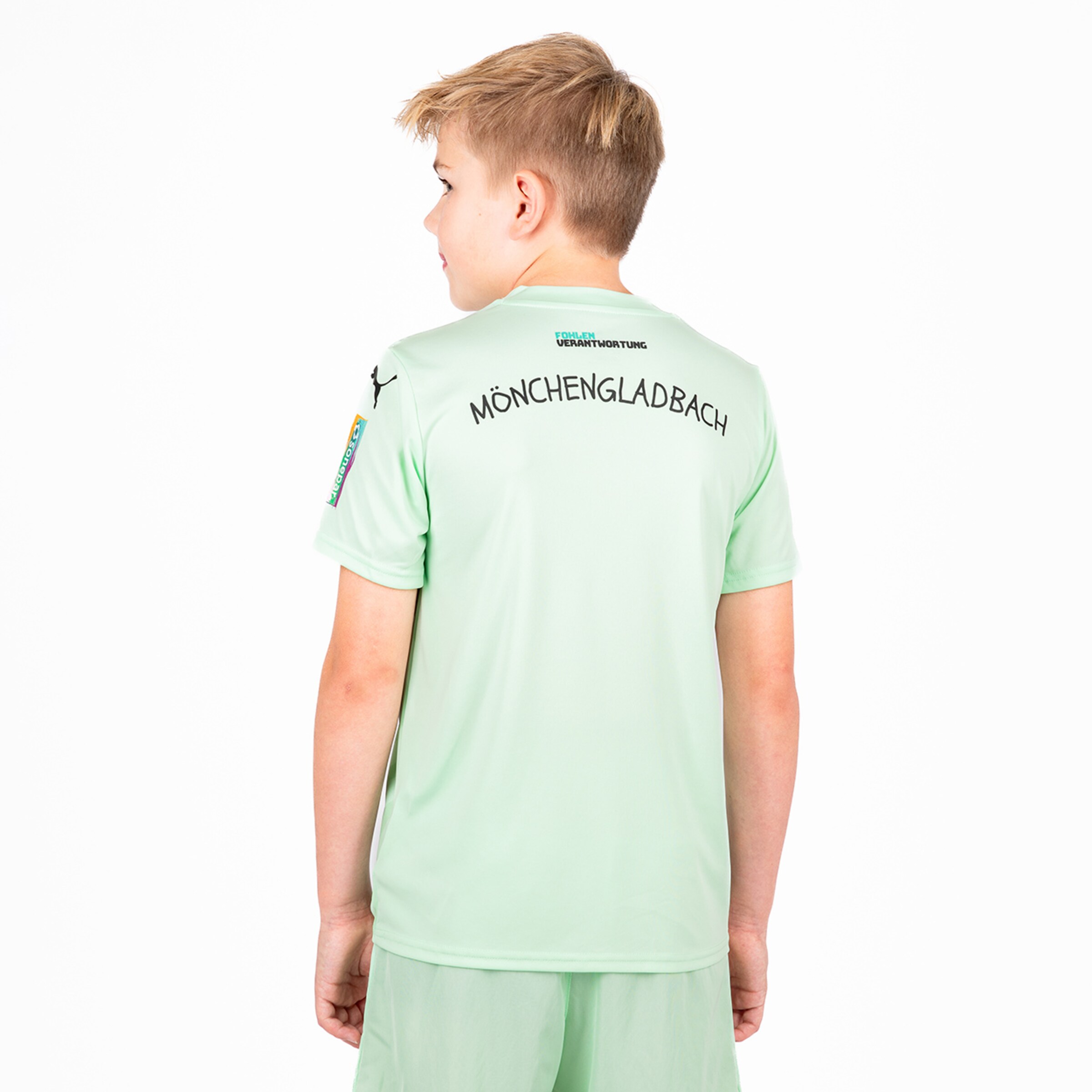 Ein Junge trägt ein grünes Borussia Mönchengladbach Trikot mit dem Schriftzug MÖNCHENGLADBACH auf dem Rücken.