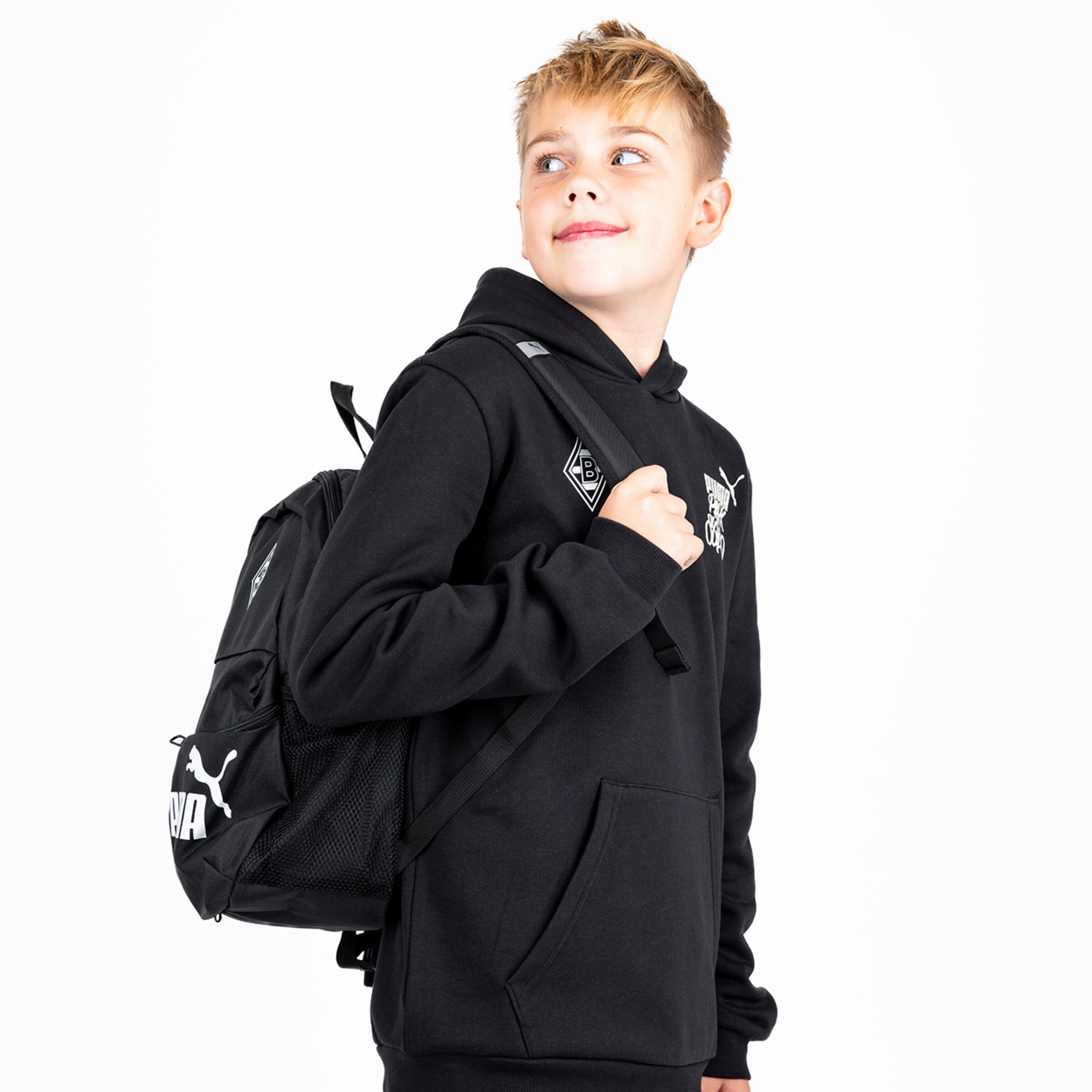 Junge trägt einen schwarzen Hoodie und einen schwarzen Rucksack. Er schaut mit lächelndem Blick zur Seite.