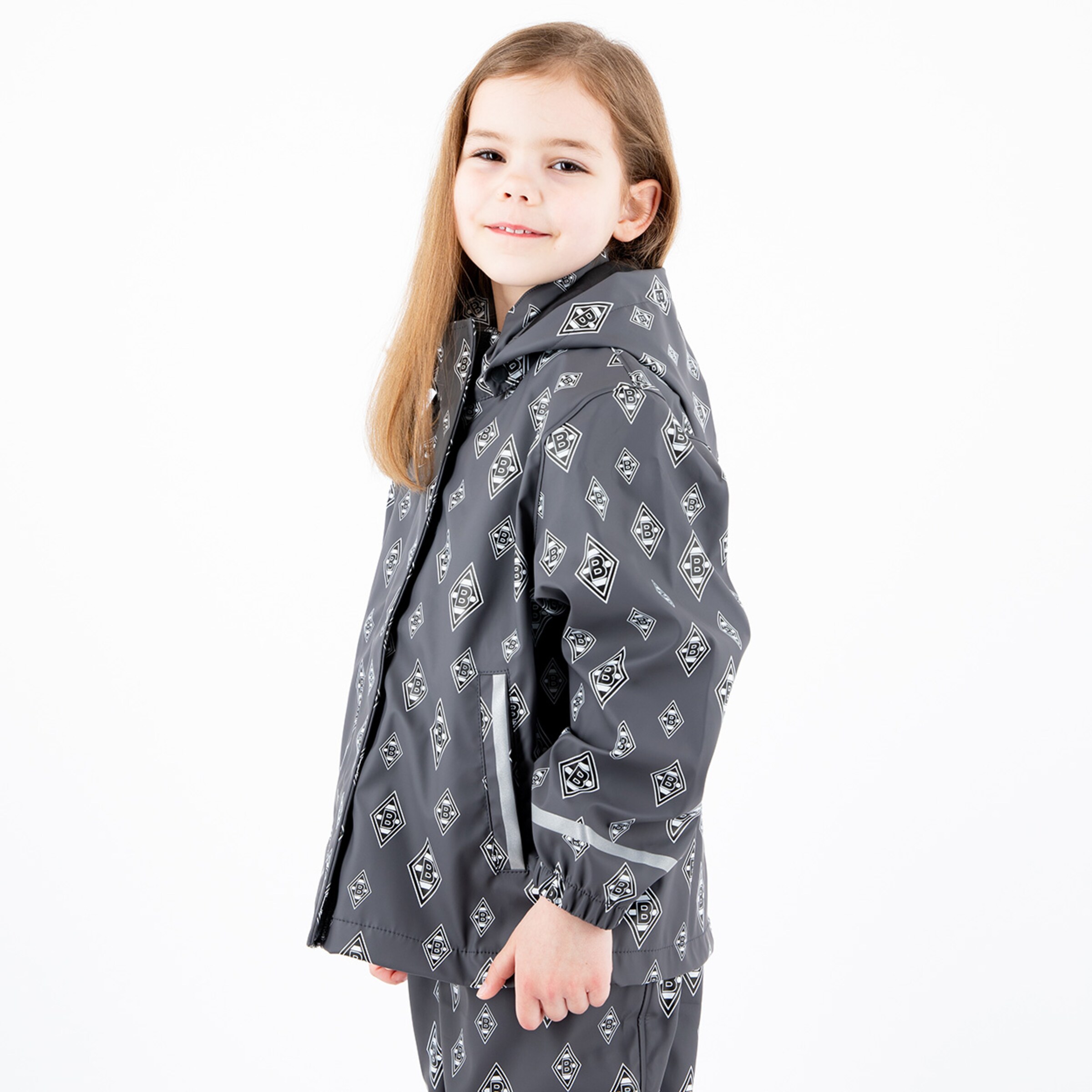 Mädchen mit langer Haaren trägt eine graue Regenjacke mit Mustern lächelt.