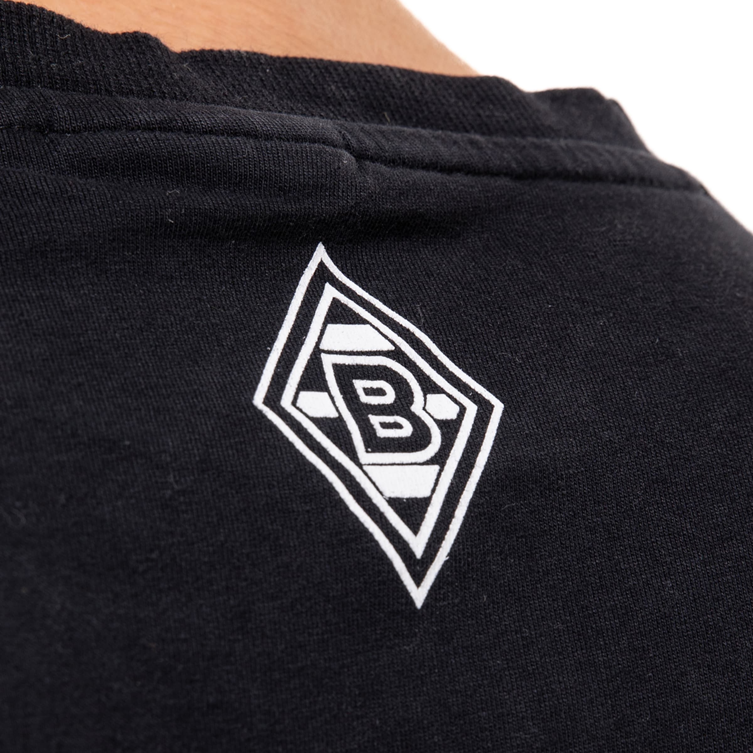 Nahaufnahme des weißen Borussia Mönchengladbach Rauten-Logos auf dem Nacken eines schwarzen T-Shirts.