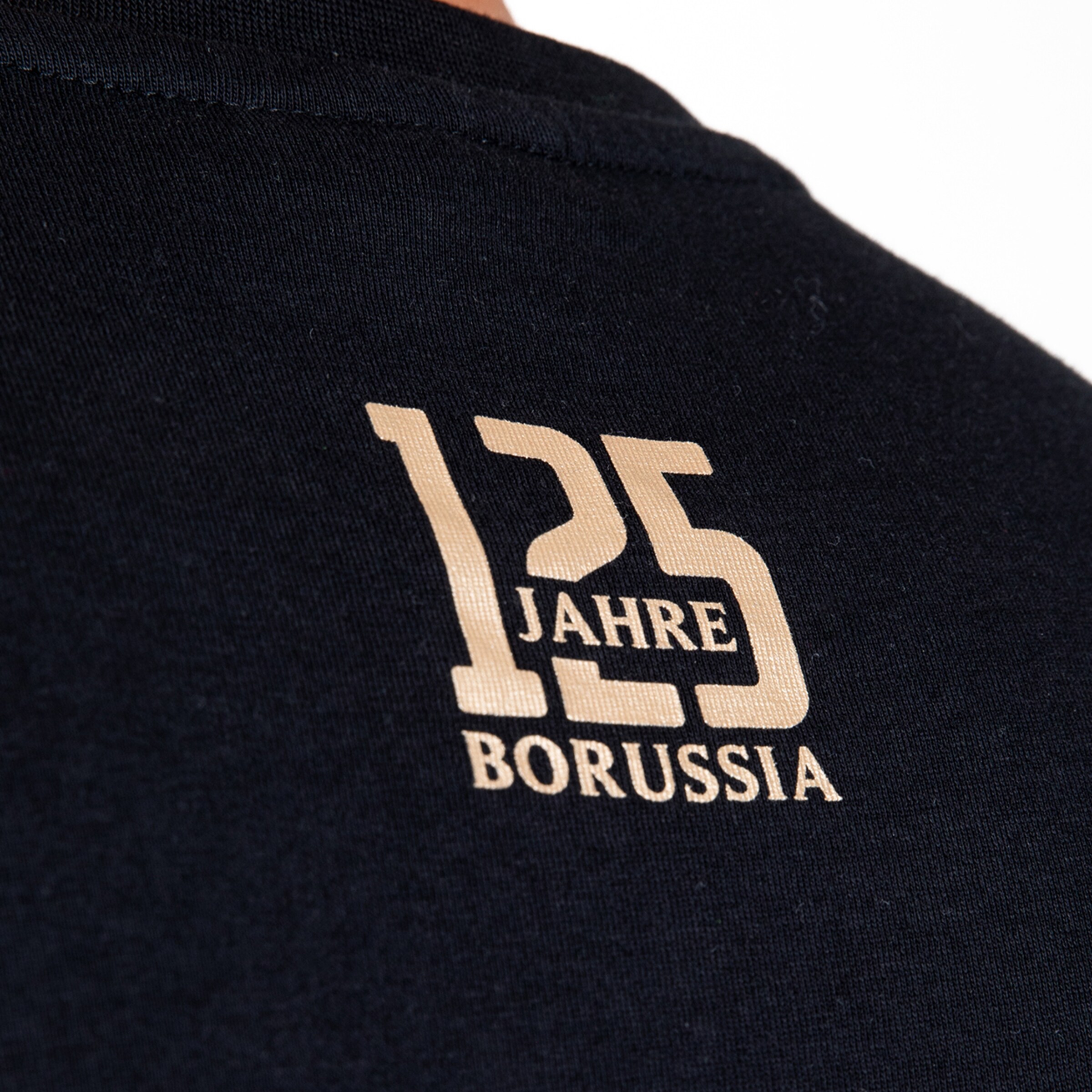 Goldener „125 JAHRE BORUSSIA“-Jubiläumsaufdruck im Nackenbereich eines schwarzen T-Shirts.