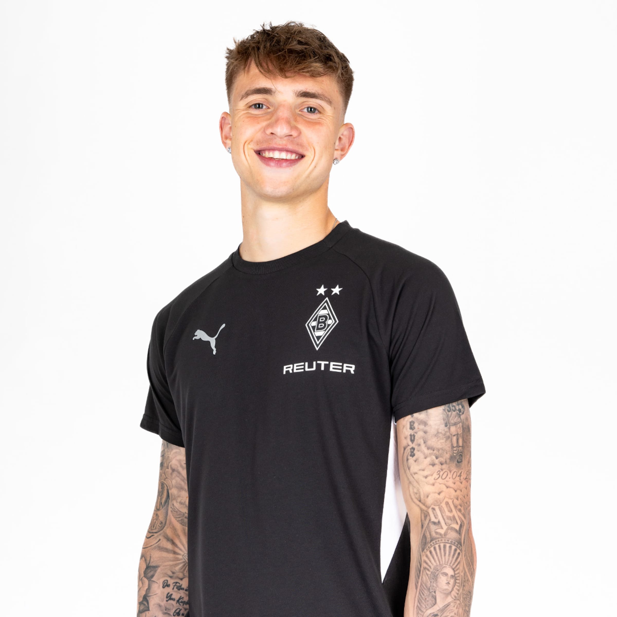 Junger Mann mit Tattoos trägt ein schwarzes T-Shirt mit Puma-Logo und Borussia Mönchengladbach-Details.