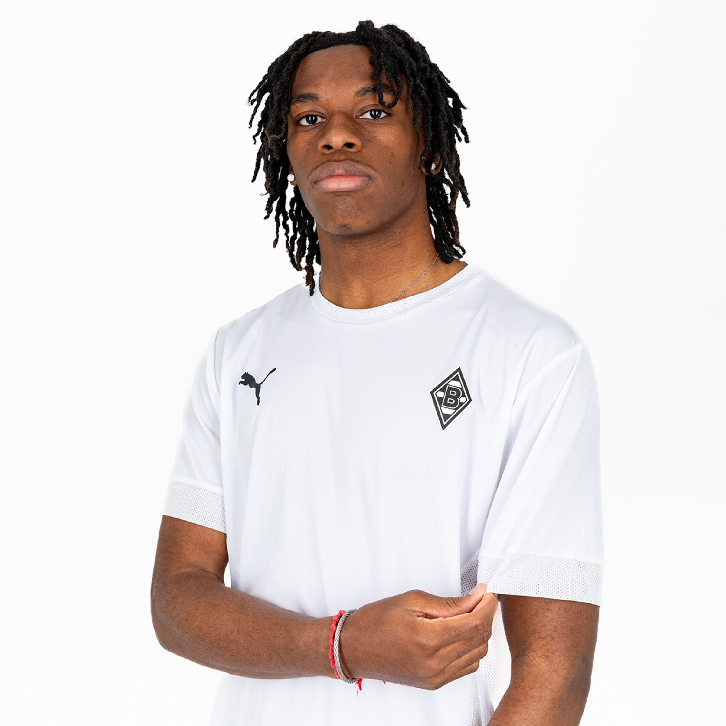 A young man with curly black hair wears a white jersey featuring the Borussia Mönchengladbach logo.