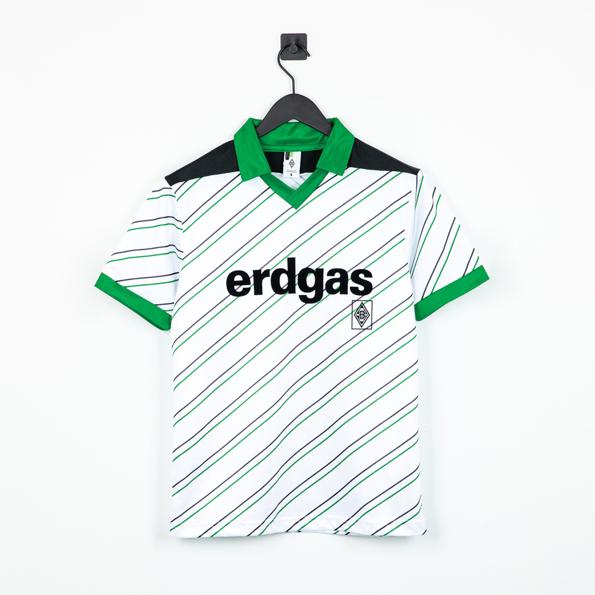 Weißes Borussia-Mönchengladbach-Trikot mit grünen Diagonalstreifen, "erdgas"-Sponsor und grünem Kragen, hängend vor weißem Hintergrund.