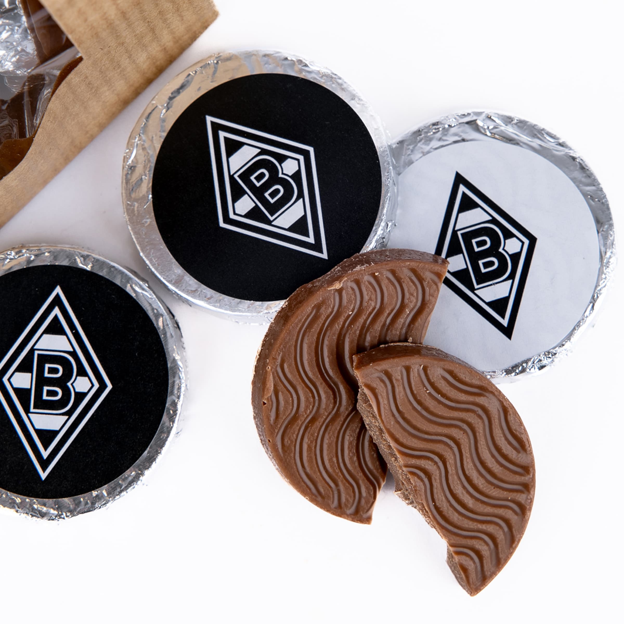 Schokoladentaler mit Borussia Mönchengladbach Logo, teils in Silberfolie verpackt, zwei zerbrochene Stücke zeigen ein Wellenmuster.
