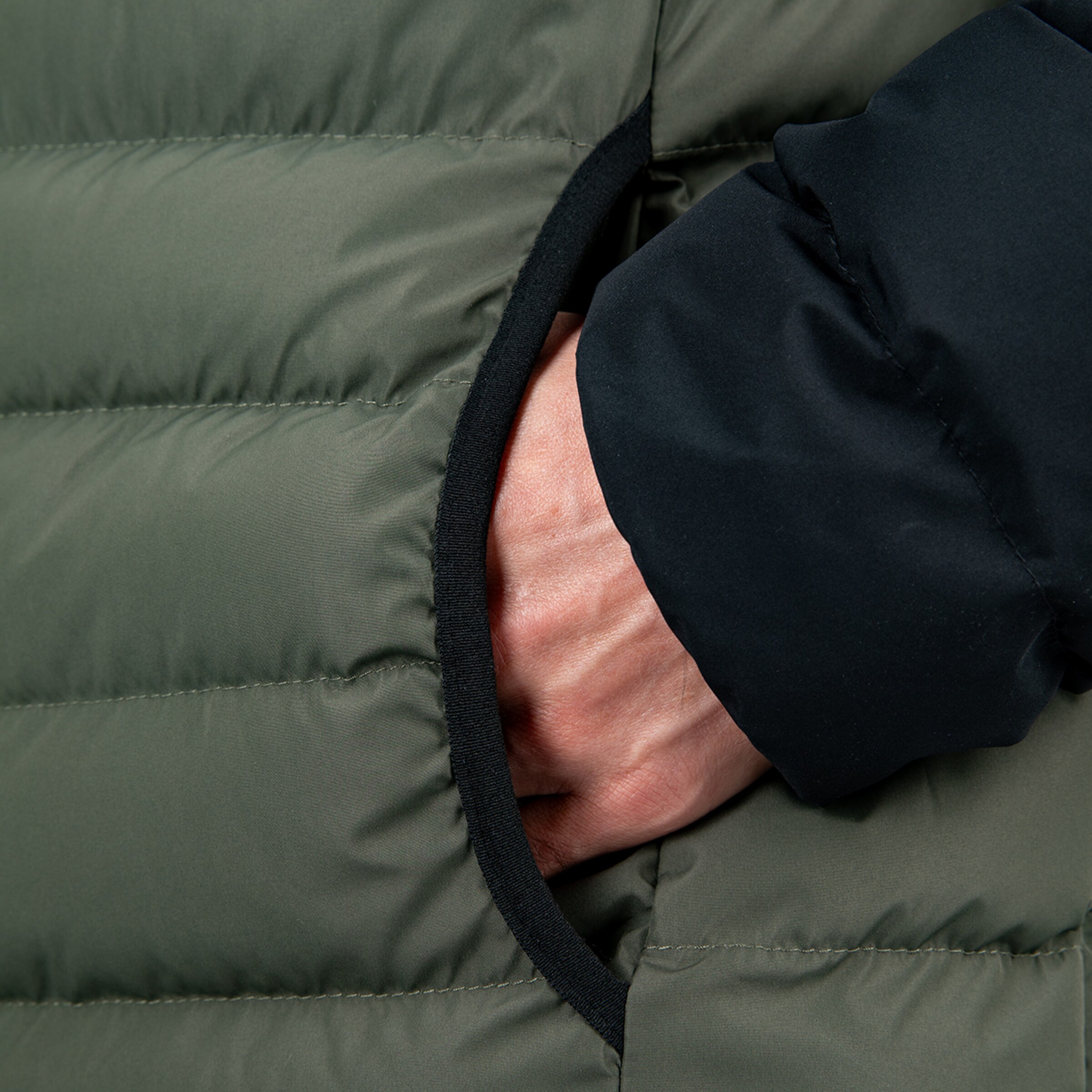 Nahaufnahme einer Hand die in die Tasche einer grünen Steppjacke greift.
