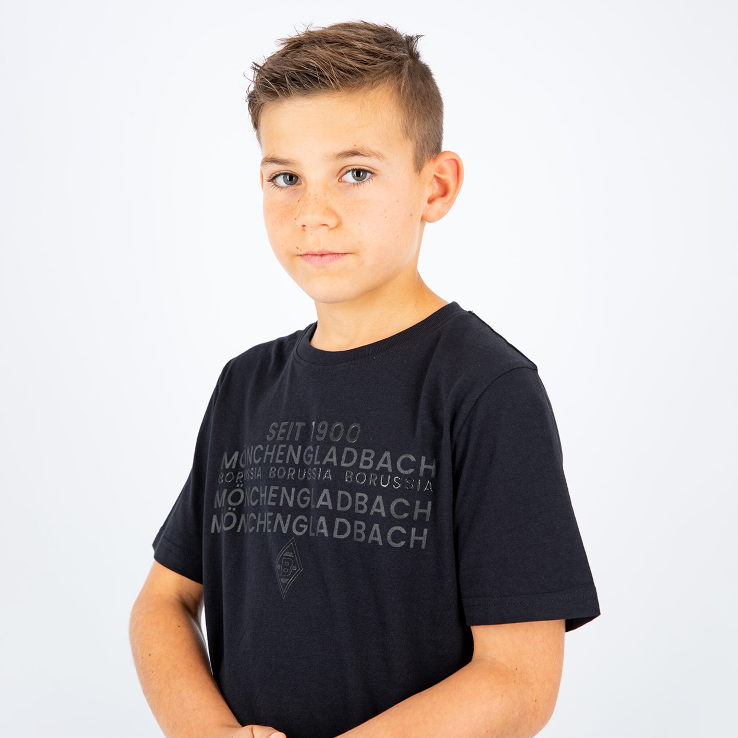 Junger Junge mit kurzem Haar trägt ein schwarzes T-Shirt mit dem Aufdruck seit 1900 Mönchengladbach.