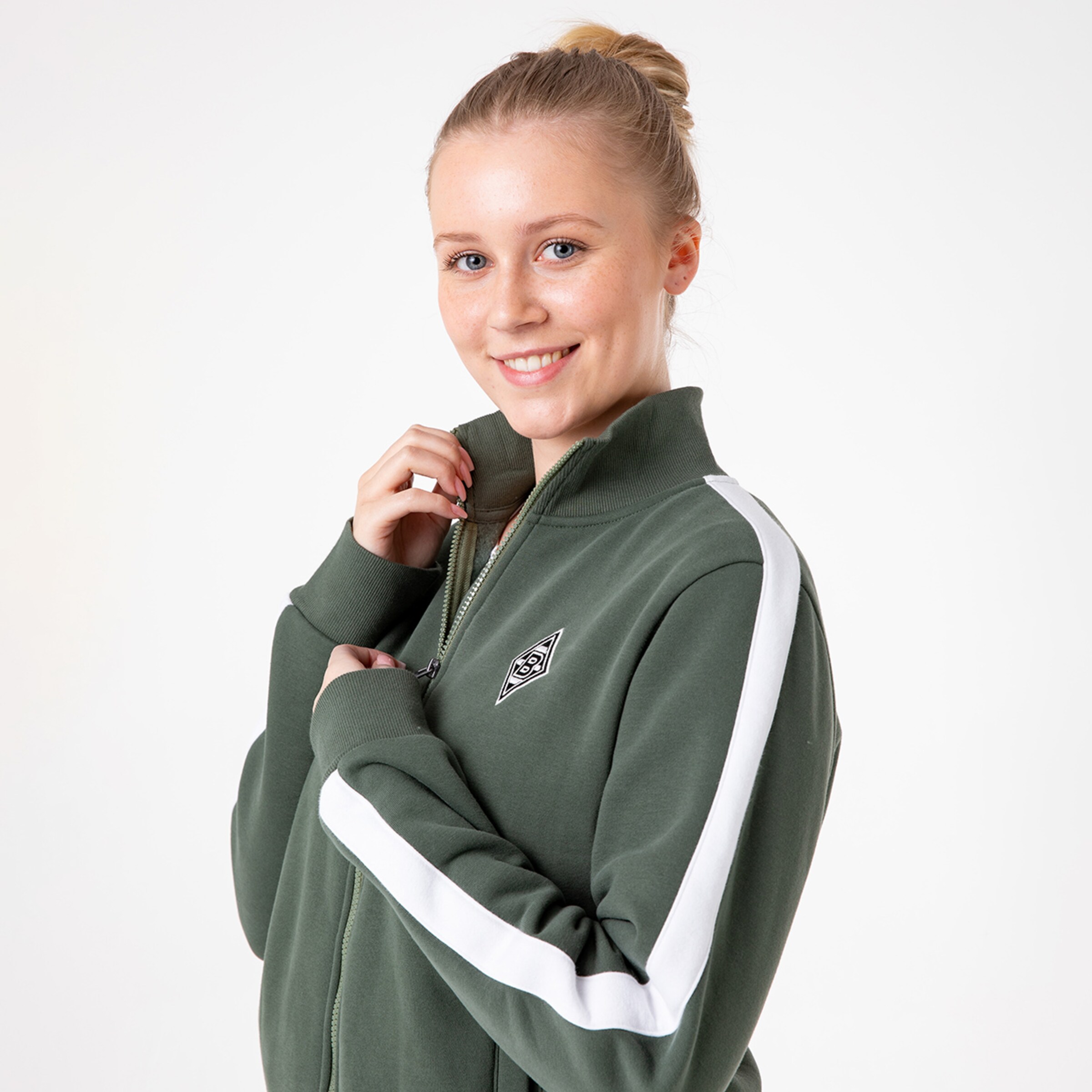 Frau mit lächelndem Gesicht trägt eine grüne Jacke mit weißen Streifen und einem Logo.