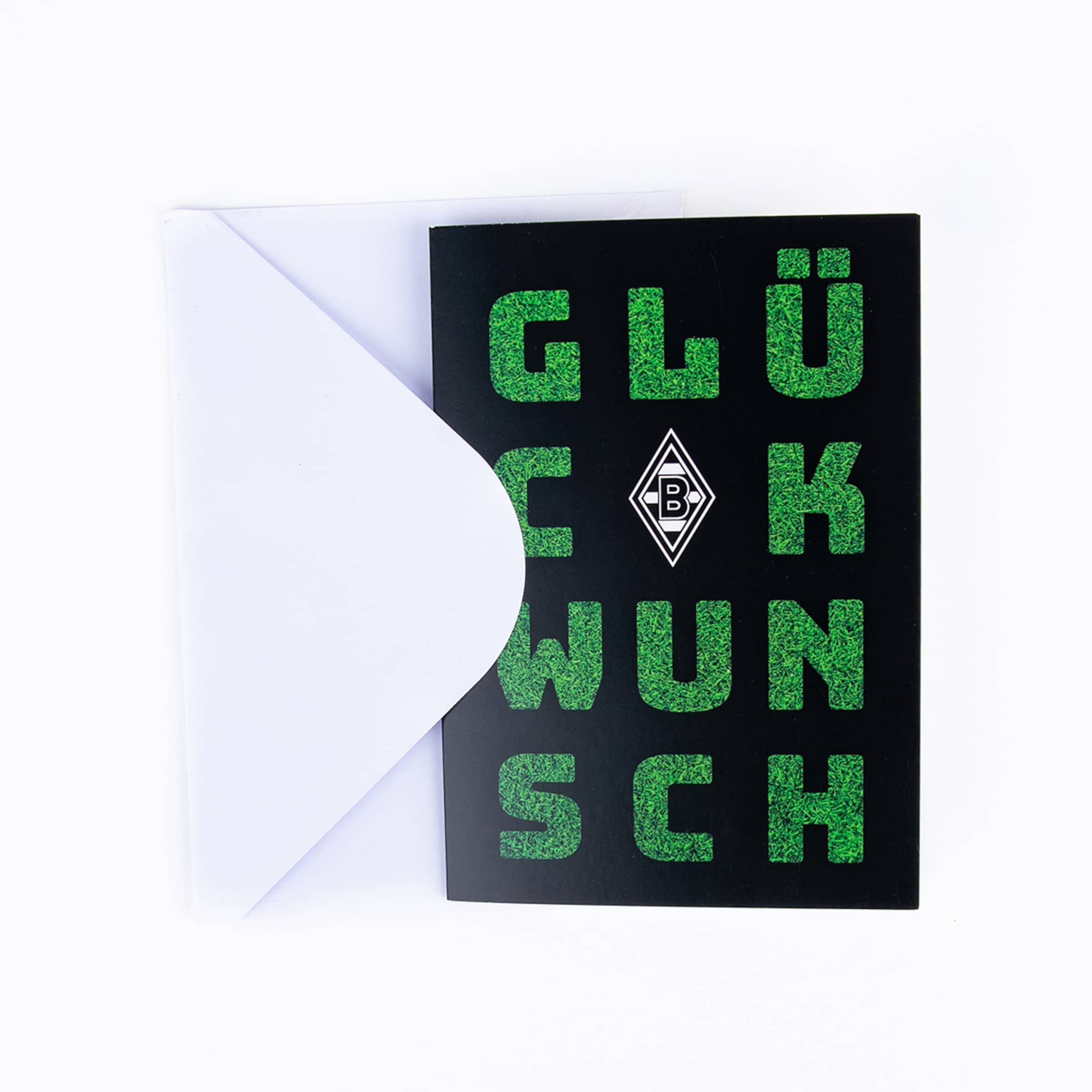 A black greeting card with green, grass-textured letters forming the word "GLÜCKWUNSCH" (Congratulations) is partially inserted into a white envelope. The white logo of Borussia Mönchengladbach is featured in the center of the card.