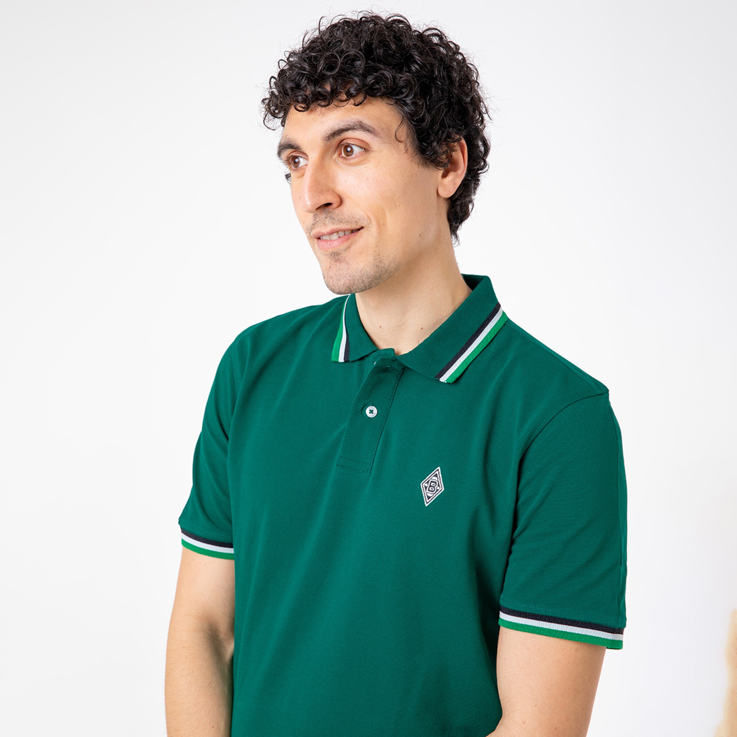 Mann in grünem Poloshirt mit Logo lächelnd und nach links schauend.