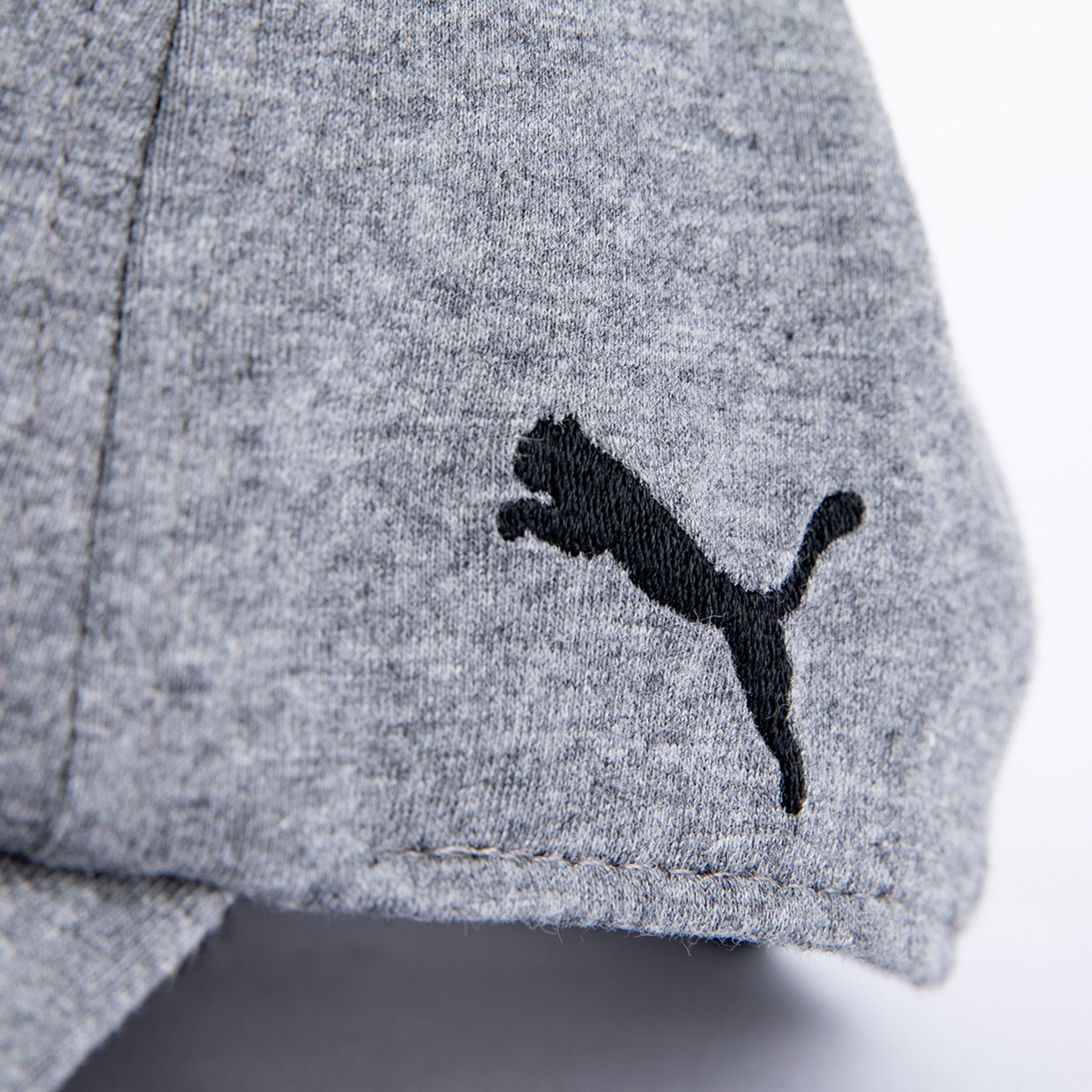 Nahaufnahme eines melierten grauen Stoffes, wahrscheinlich von einer Kappe oder einem Sweatshirt, mit einem schwarz gestickten Puma-Logo, das die Silhouette eines springenden Pumas darstellt.