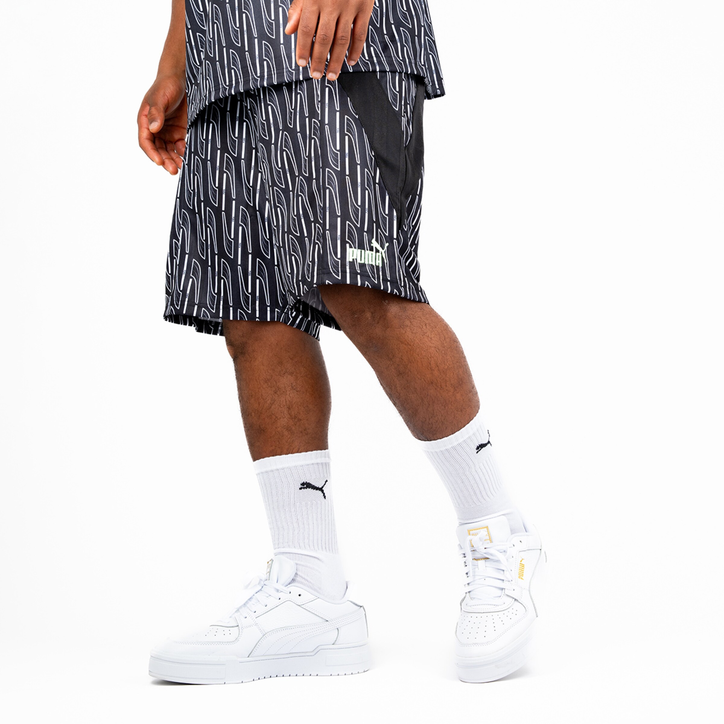 Schwarze Sportshorts mit grafischem Muster und Logo von Puma kombiniert mit weißen Sneakers.