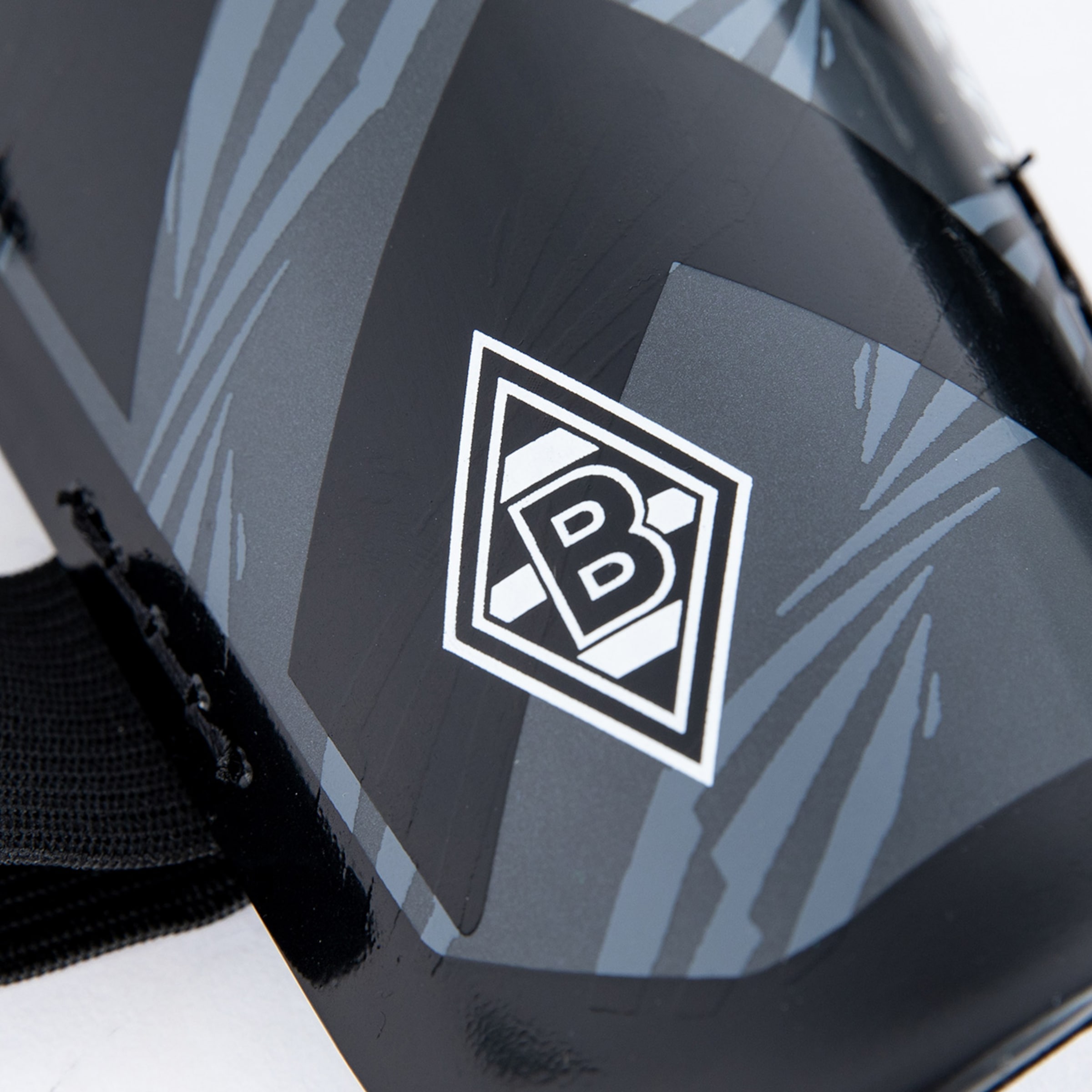 Nahaufnahme eines schwarzen Schienbeinschoners mit dem Logo von Borussia Mönchengladbach (ein "B" in einer Raute).