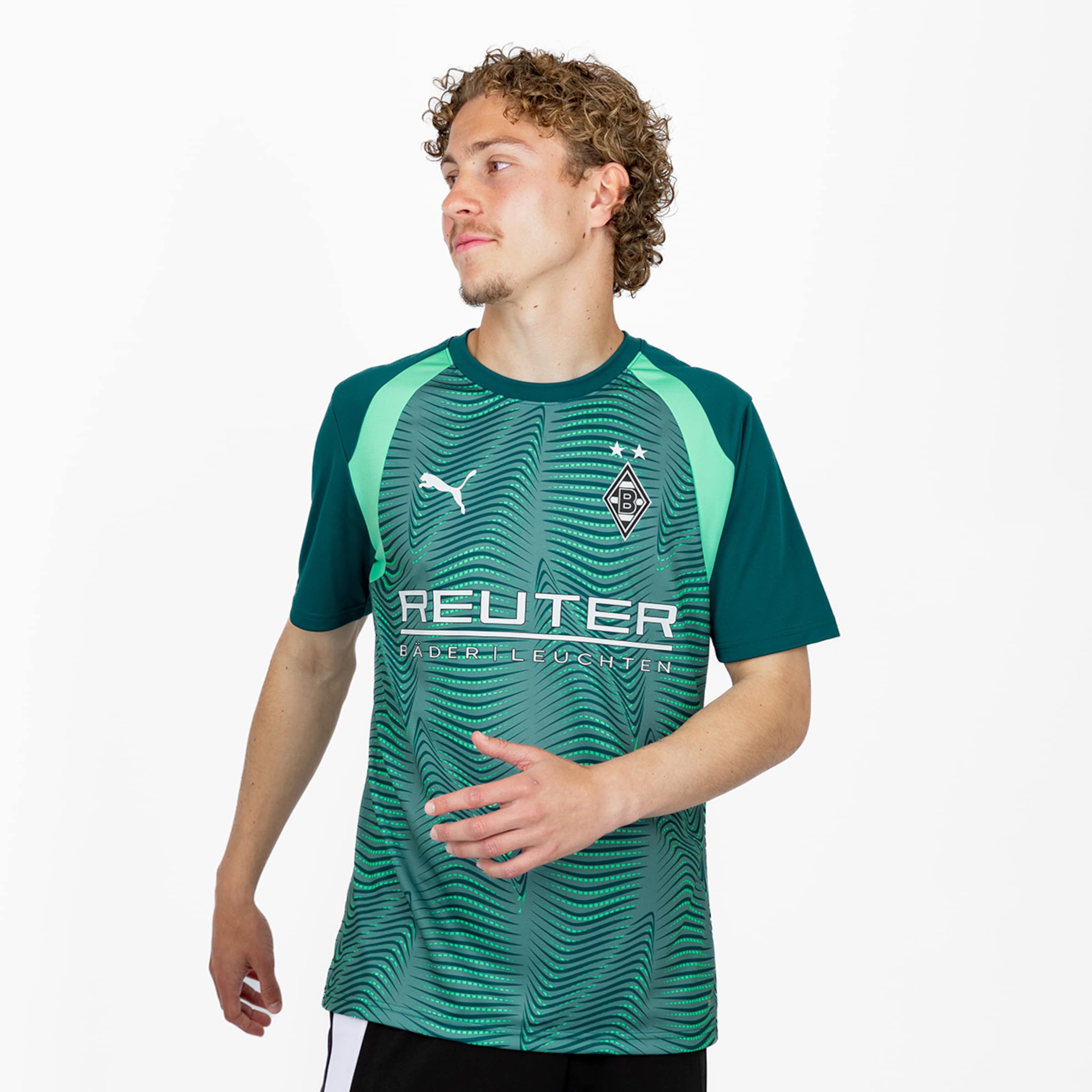 Junger Mann mit lockigem Haar in grünem Borussia Mönchengladbach Trikot mit REUTER-Sponsor vor weißem Hintergrund. Das Trikot hat ein wellenförmiges Muster.