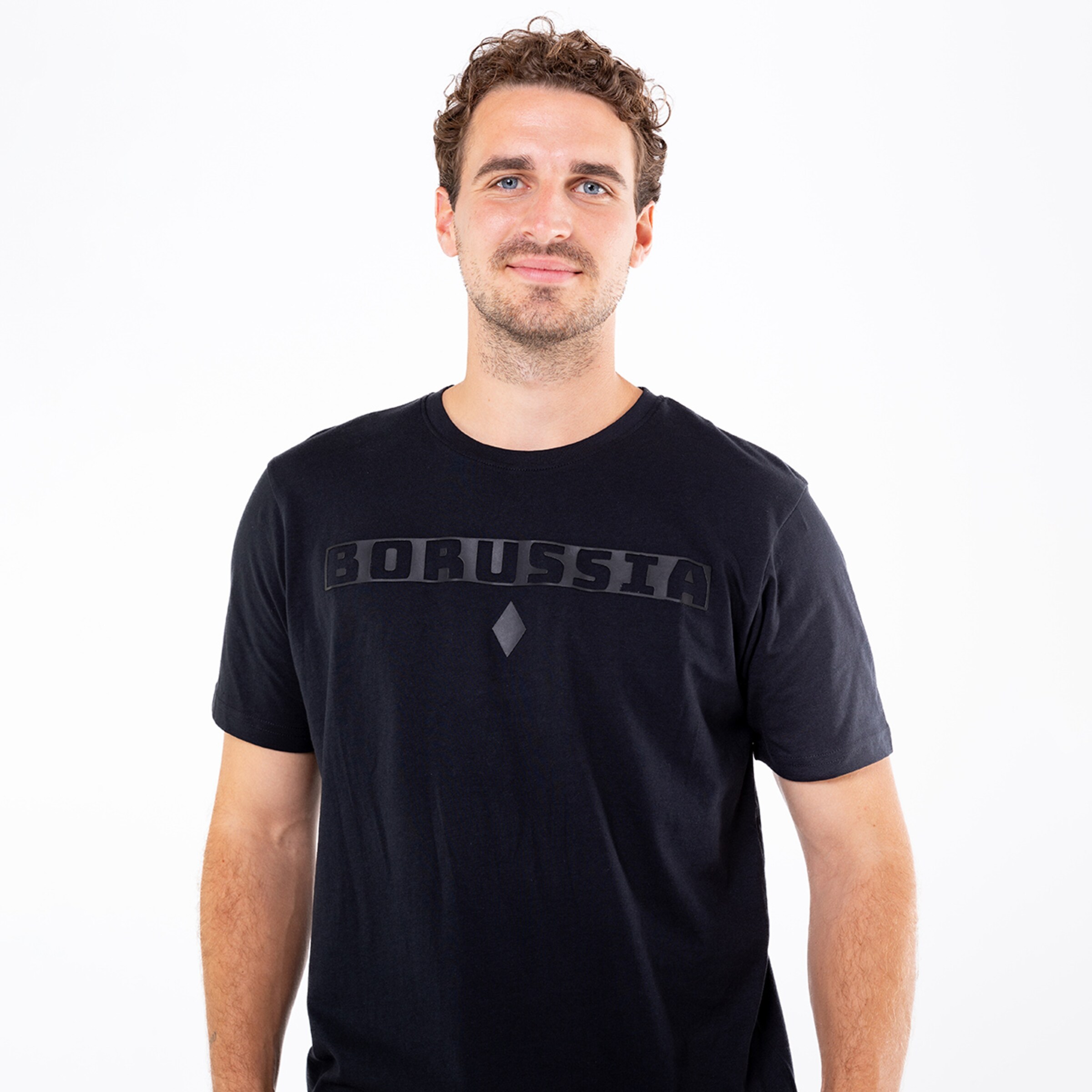 Ein Mann mit lockigem Haar trägt ein schwarzes T-Shirt mit dem Schriftzug BORUSSIA.