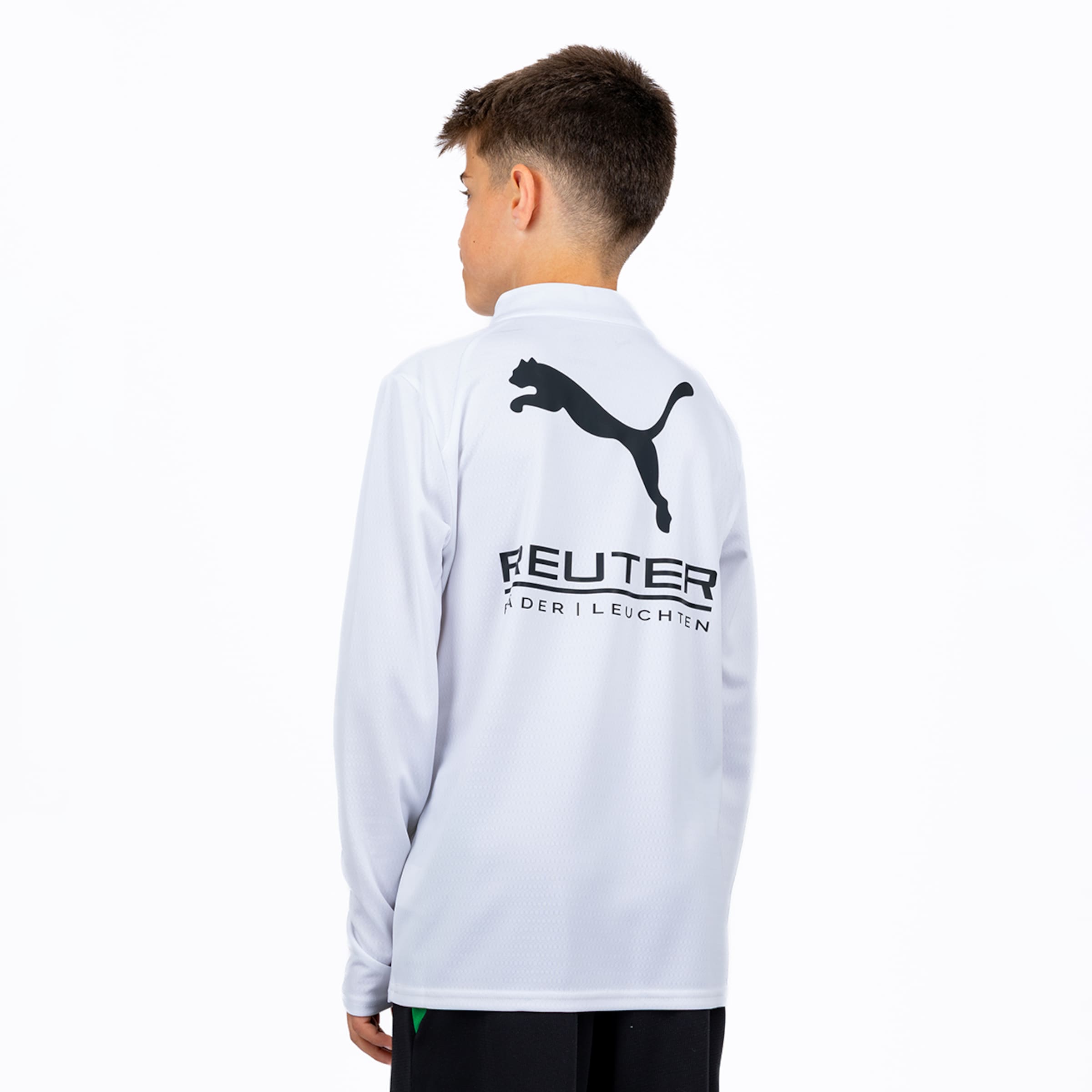 Ein Junge von hinten trägt ein weißes Langarmshirt mit einem schwarzen Puma-Logo und dem Schriftzug "FEUTER ÄDER | LEUCHTEN". Er hat dunkelbraunes, kurz geschnittenes Haar und trägt schwarze Hosen.