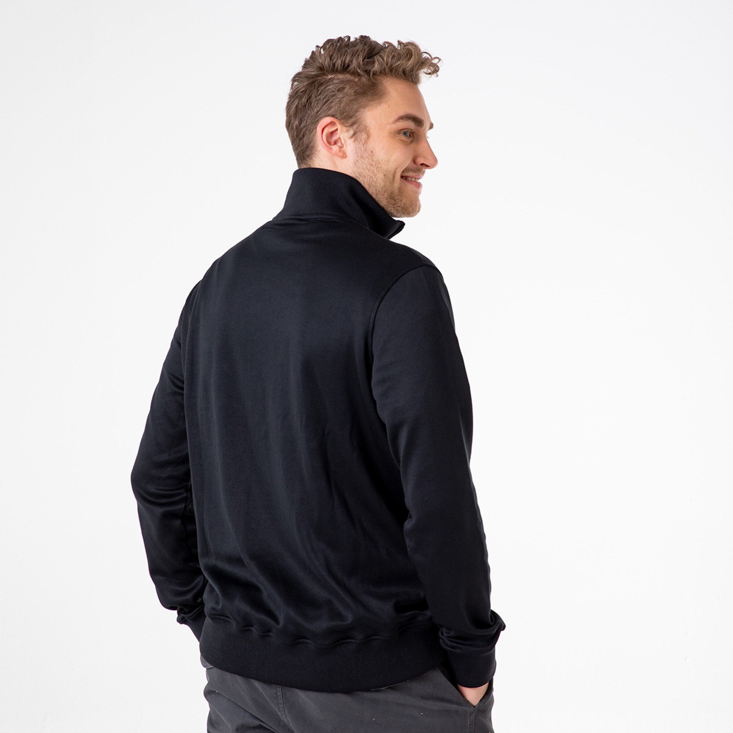 Person mit lockigem Haar trägt einen schwarzen Pullover mit Stehkragen von hinten aufgenommen.