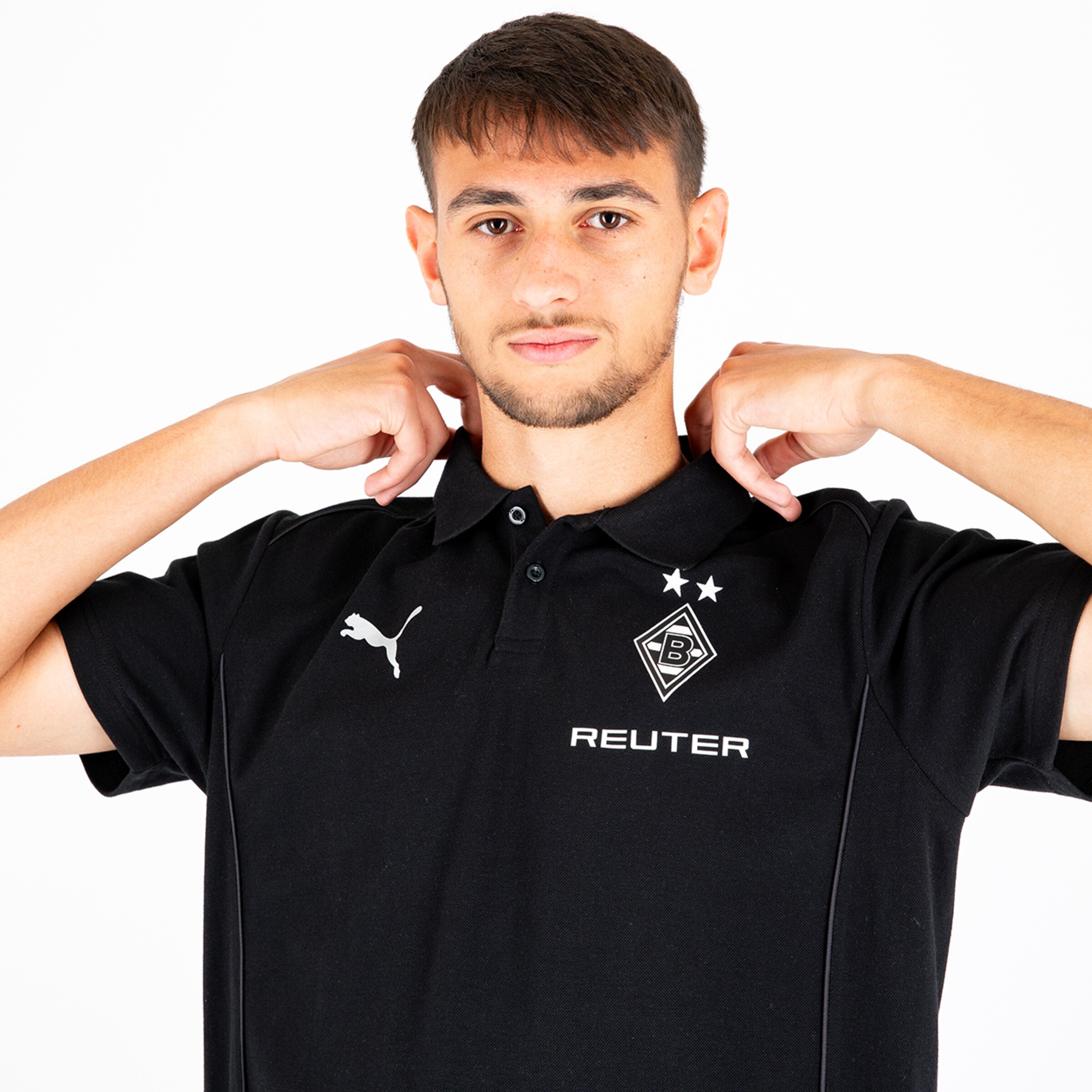 Ein junger Mann in einem schwarzen Polo mit Puma-Logo und Borussia Mönchengladbach-Emblem der seinen Kragen anpasst.
