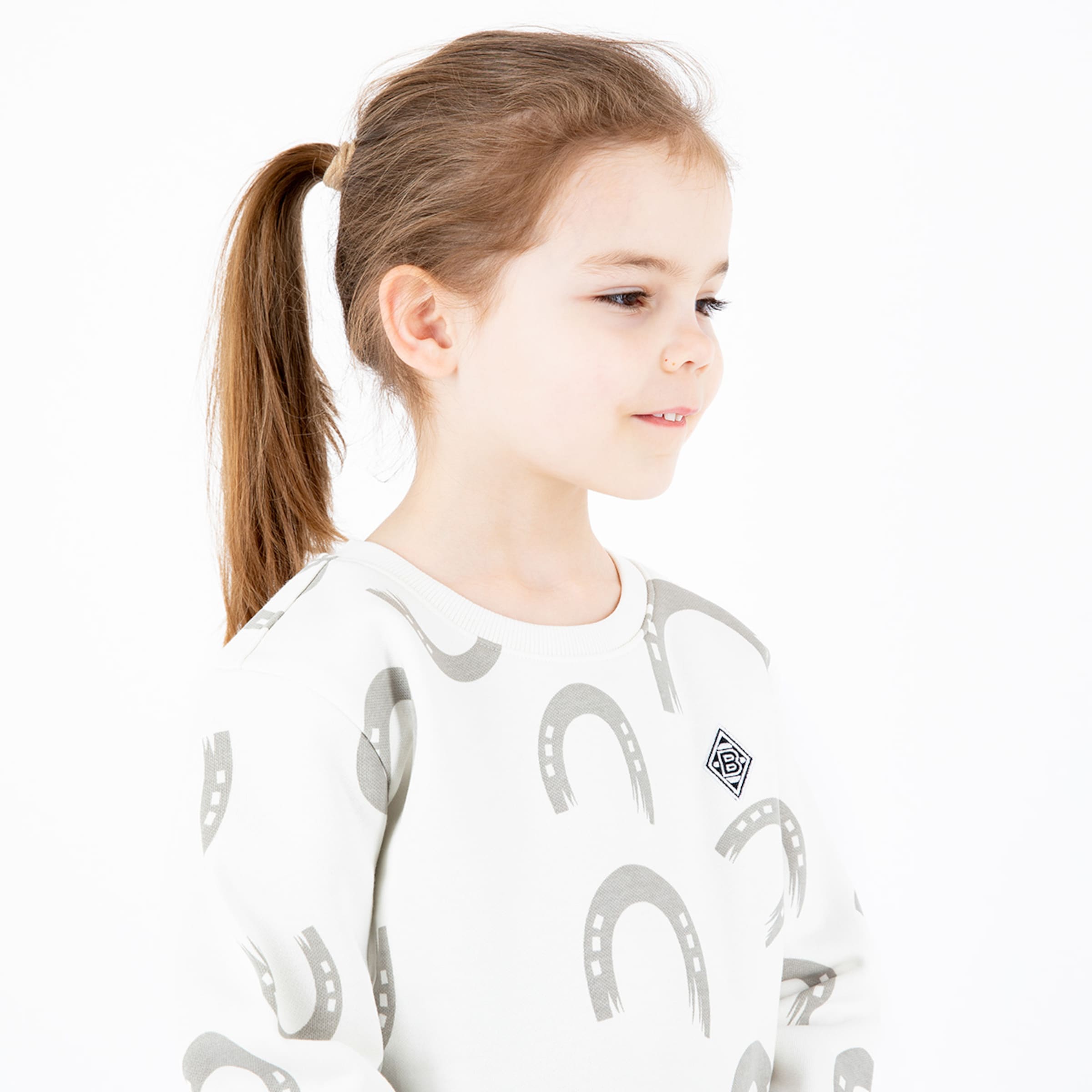 A girl with long brown hair wearing a light sweater featuring a repeated horseshoe pattern.