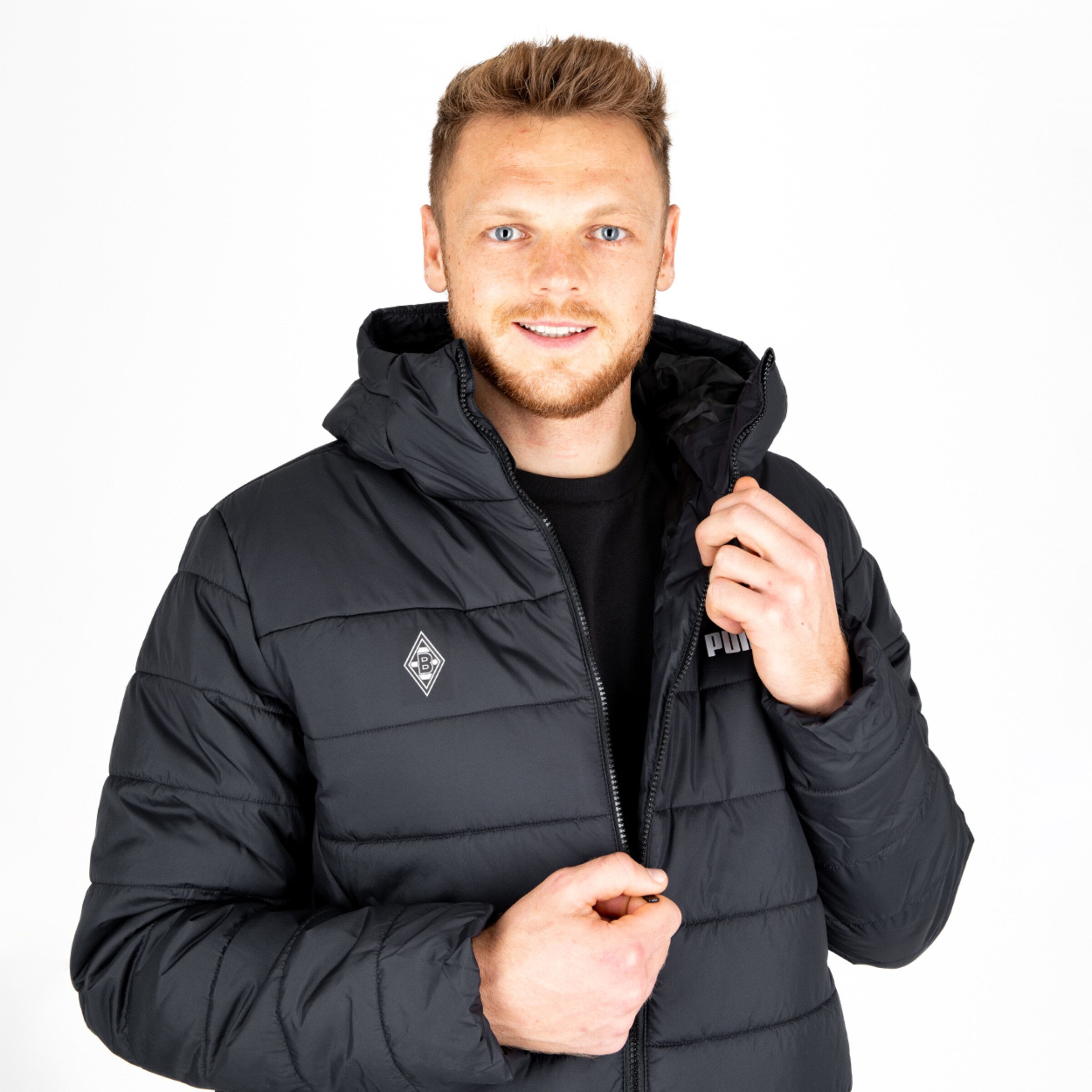 A smiling man wearing a black puffer jacket is unzipping it.
