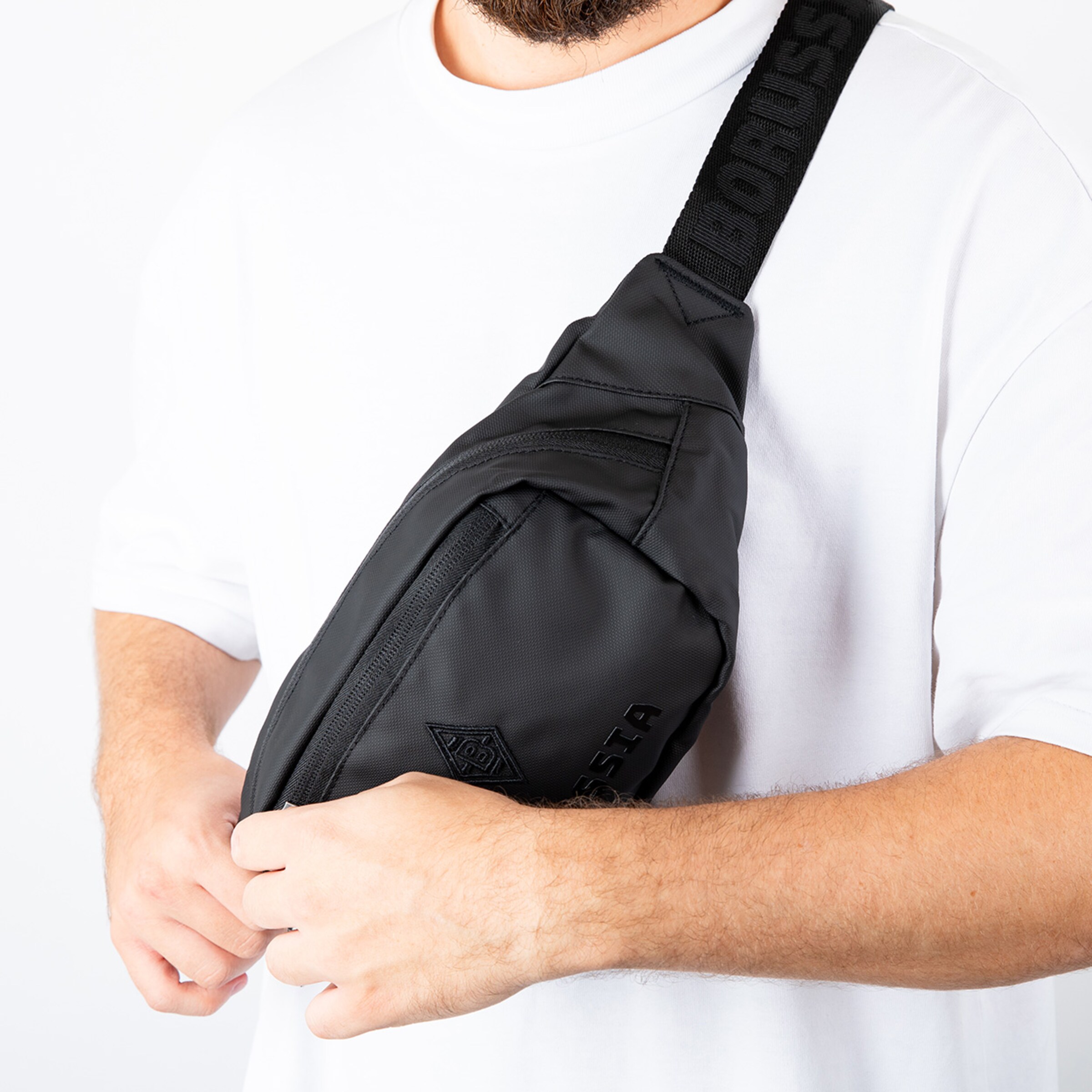 Black sling bag with logo worn by a person.