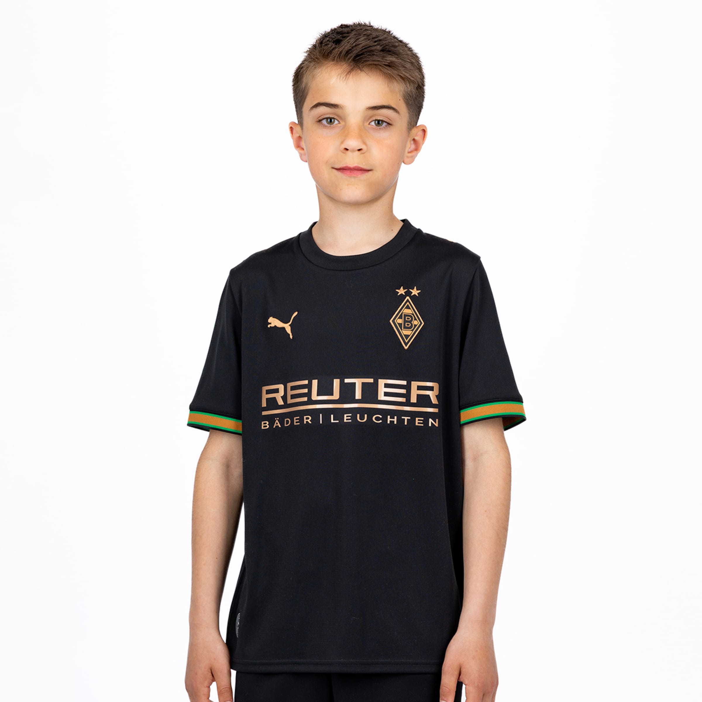 Ein Junge im schwarzen Borussia Mönchengladbach Puma Trikot mit kupferfarbenem REUTER Logo auf weißem Hintergrund.