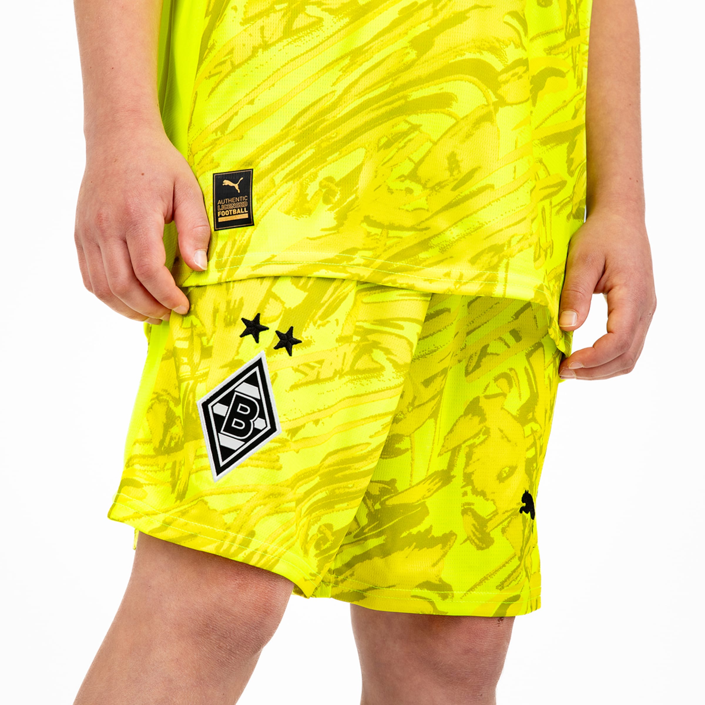 Ein Spieler trägt ein leuchtend gelbes Fußballtrikot und Shorts mit dem Logo von Borussia Mönchengladbach.