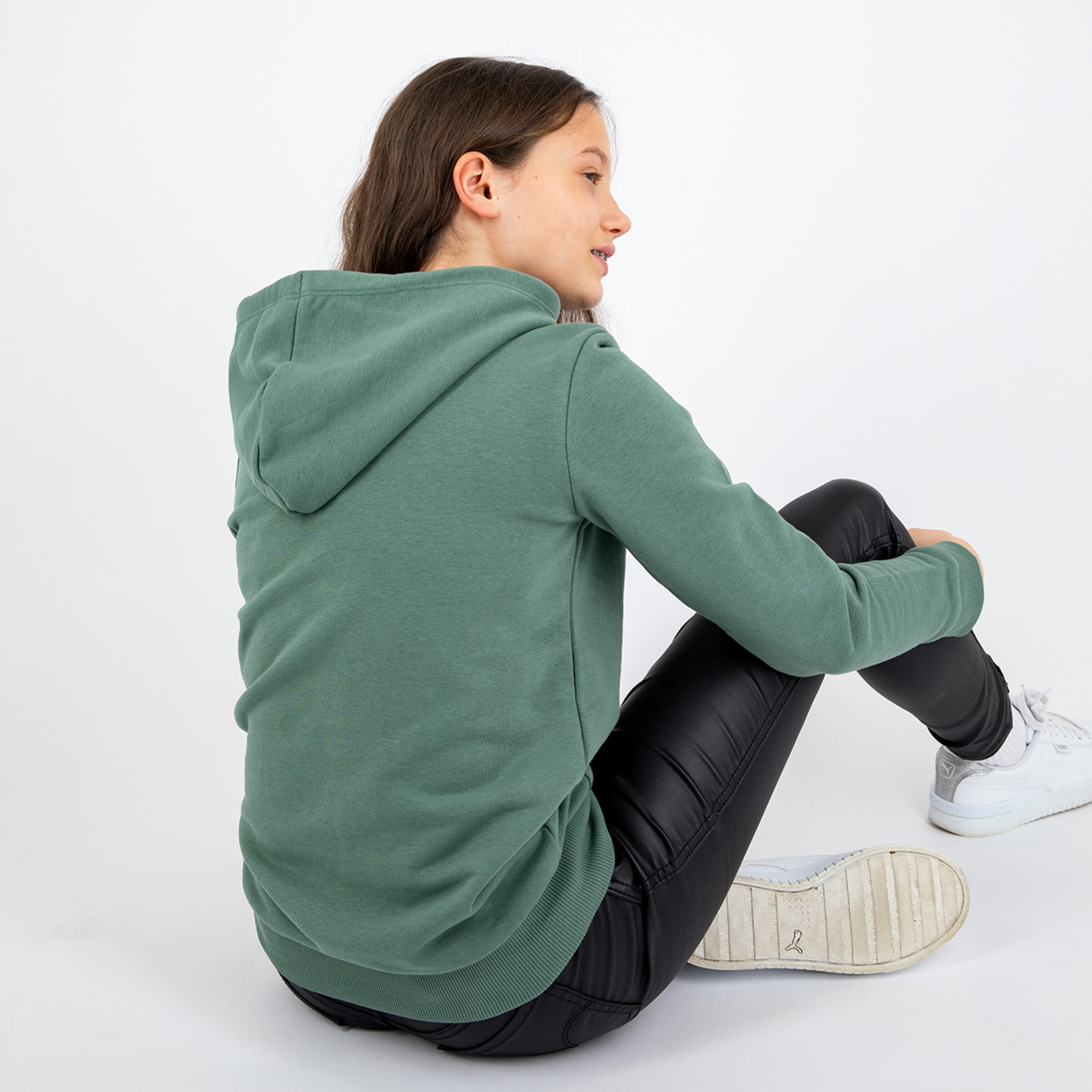 Jugendliche trägt einen kapuzenpullover und sitzt auf dem Boden.