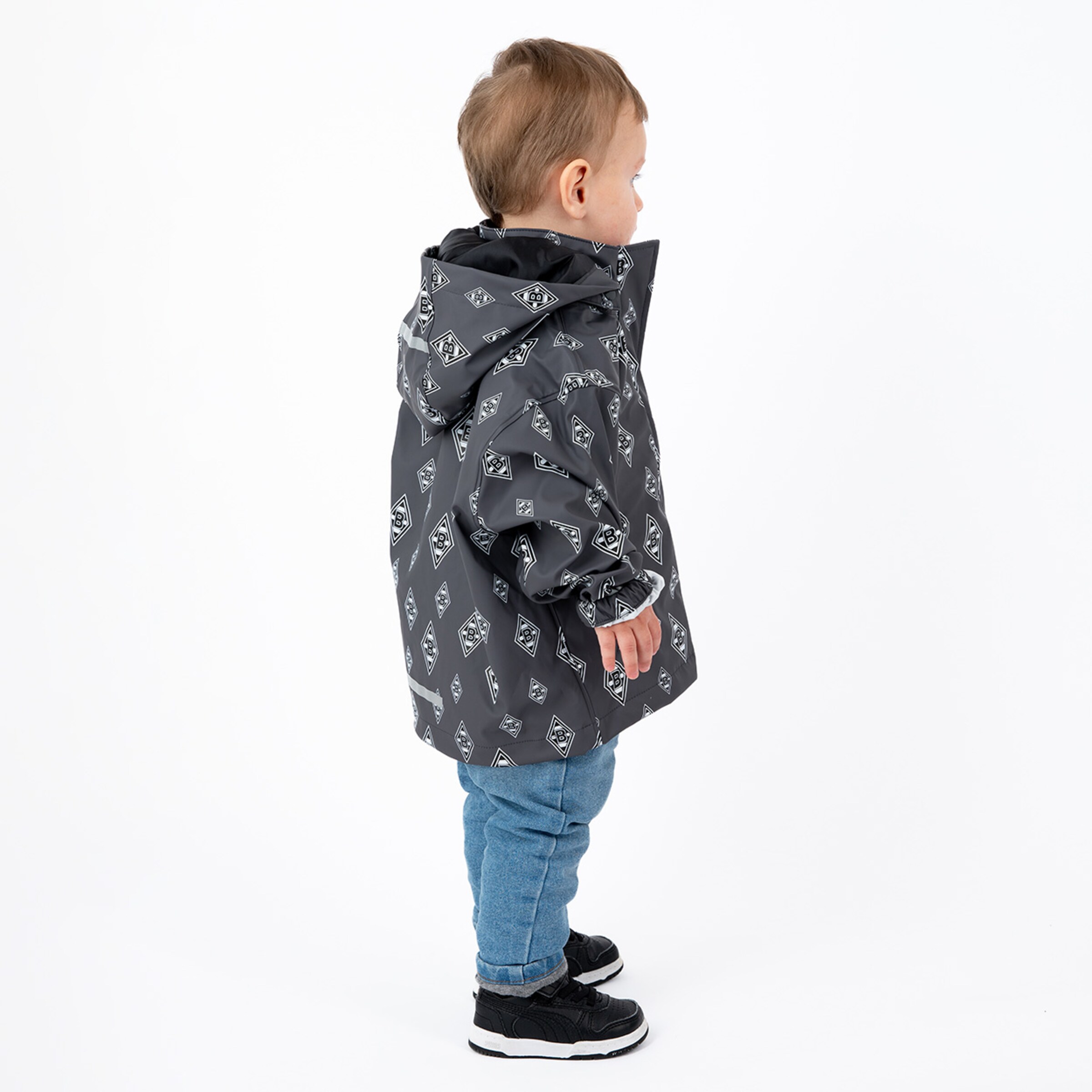 Kind trägt eine graue Jacke mit Muster und Jeans steht seitlich.