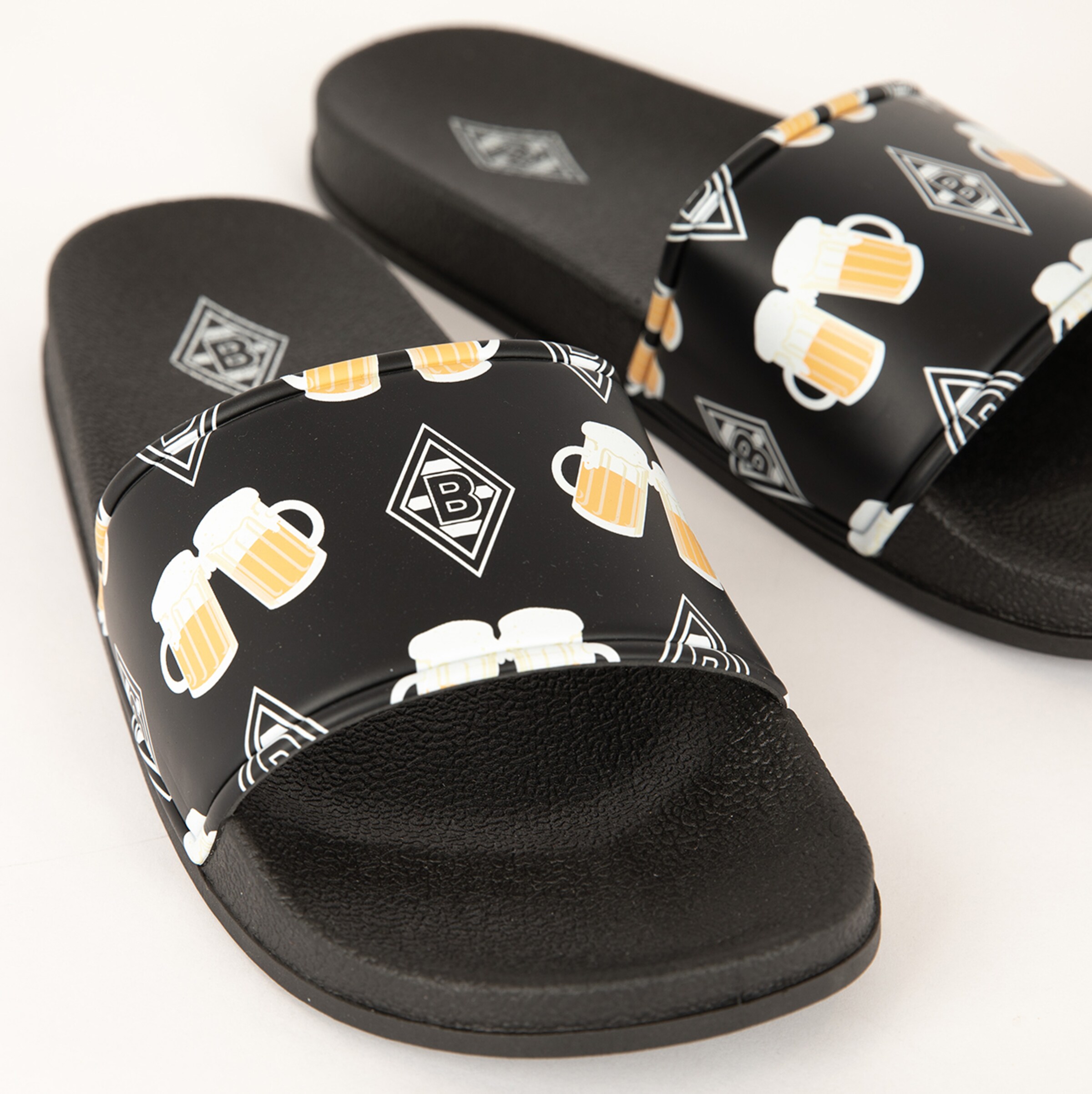 Schwarze Badeschuhe mit Bier-Motiv und Borussia Mönchengladbach-Logo.