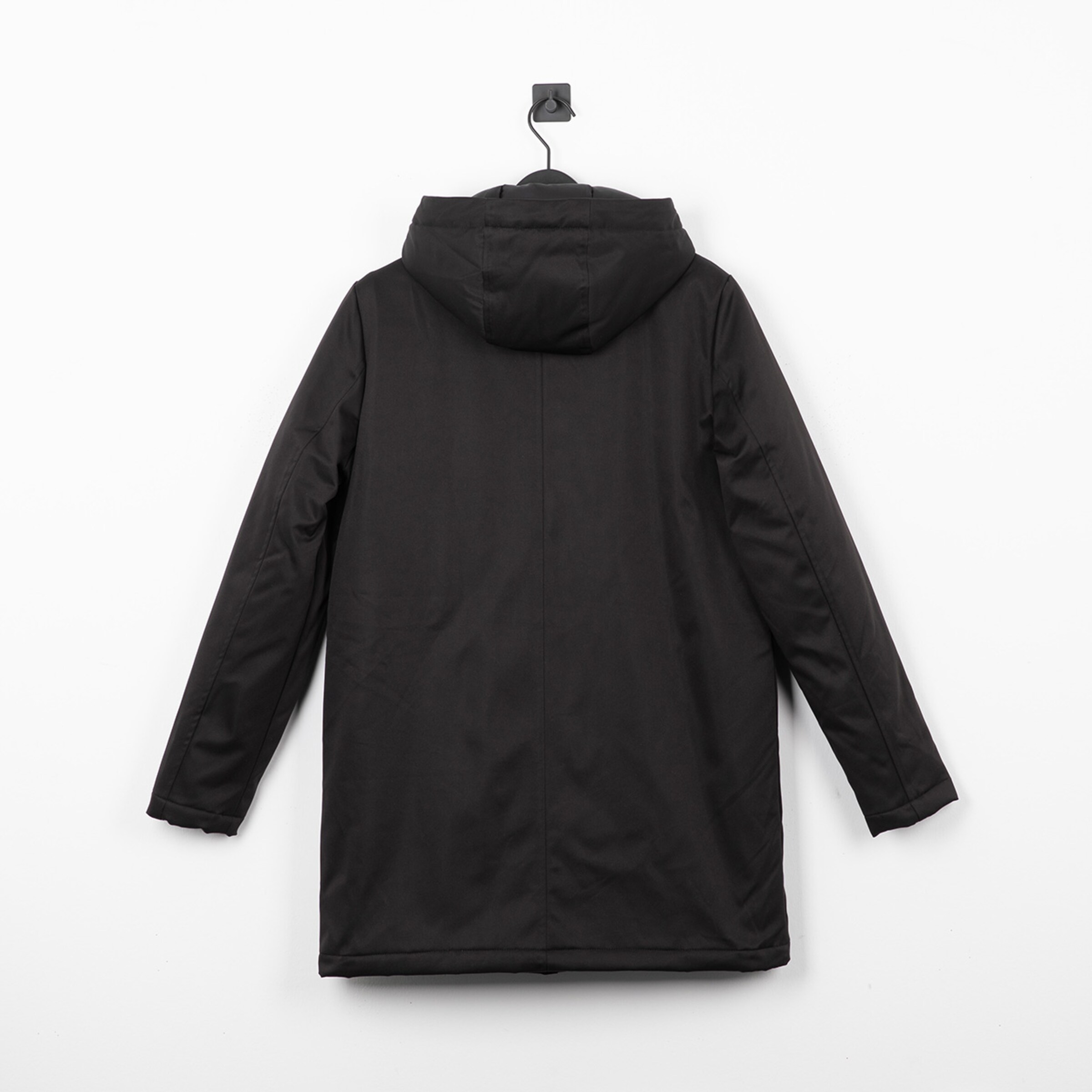 Schwarze Jacke mit Kapuze von hinten fotografiert hängt an einem Haken.