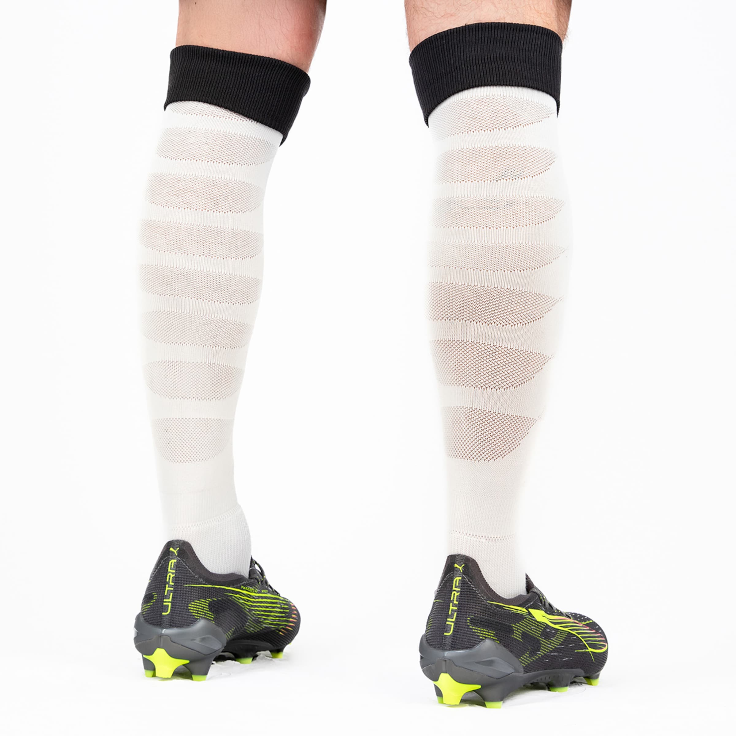Pair of white soccer socks with striped design and black cuffs paired with soccer cleats.