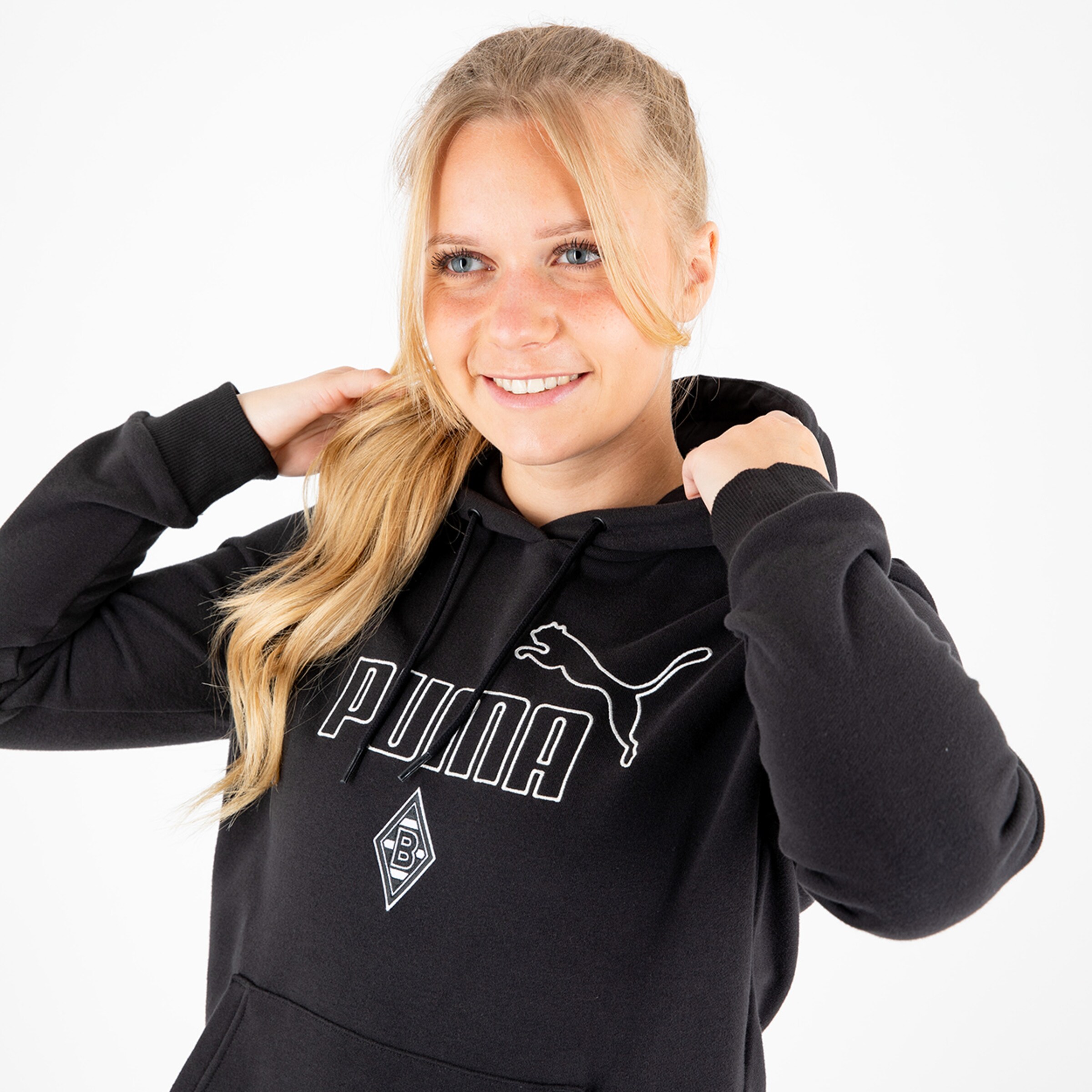 Eine lächelnde Frau mit langen blonden Haaren trägt einen schwarzen Hoodie mit dem Puma-Logo und dem Borussia Mönchengladbach-Emblem.